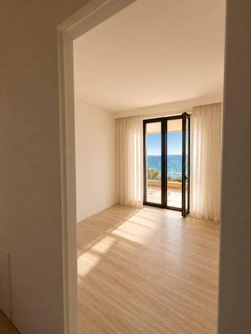 Helles Schlafzimmer mit großen Fenstern, Vorhängen und direktem Meerblick.