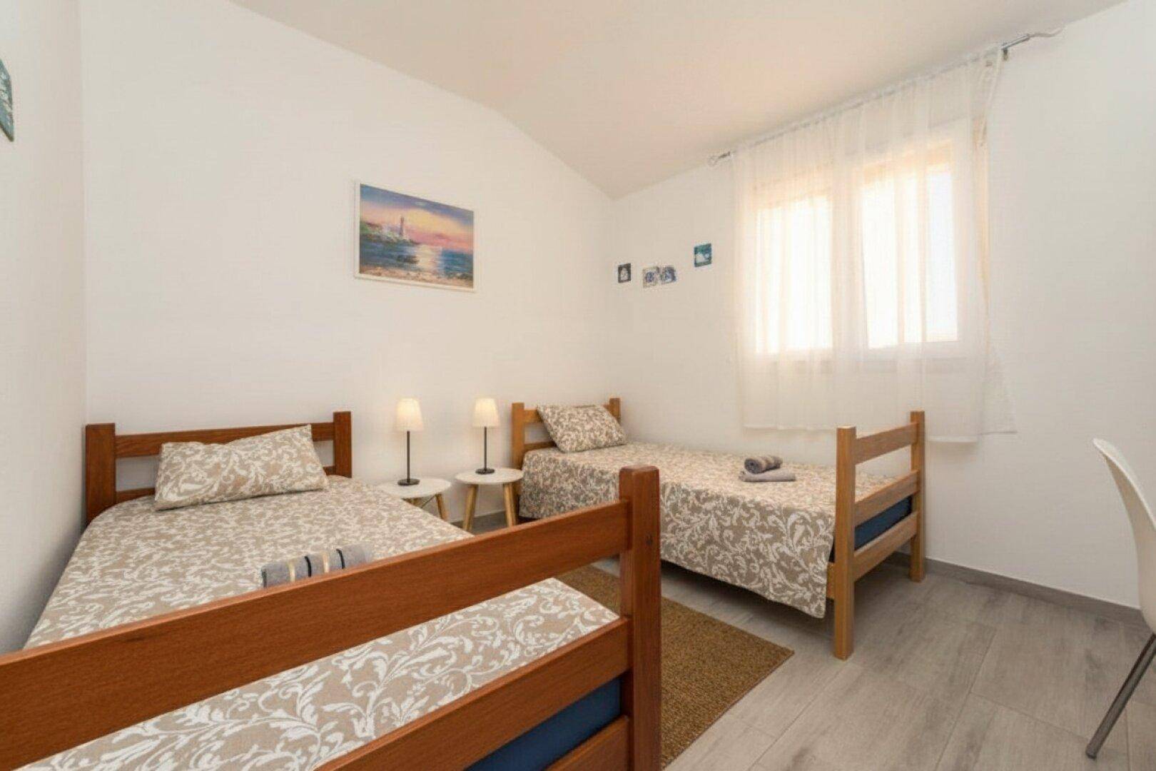 Helles Schlafzimmer mit zwei Einzelbetten, einem Fenster und schlichter, freundlicher Einrichtung.
