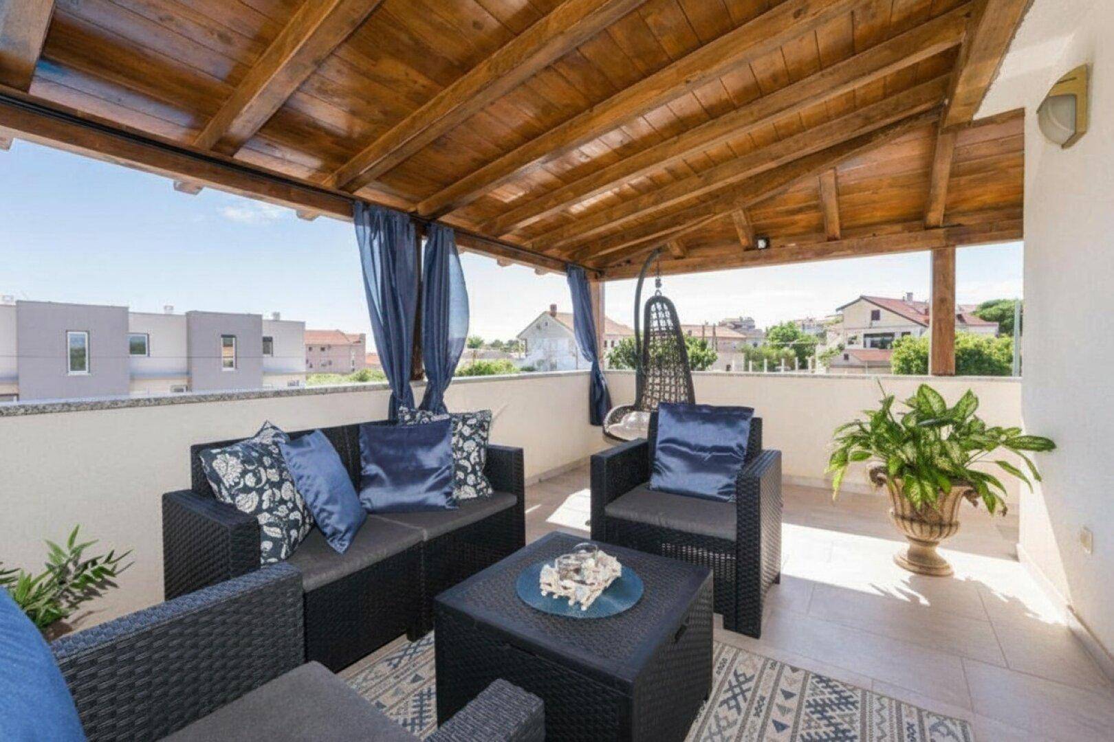Gemütliche Dachterrasse mit Holzpergola, bequemen Sitzmöbeln und Blick über die Nachbarschaft.