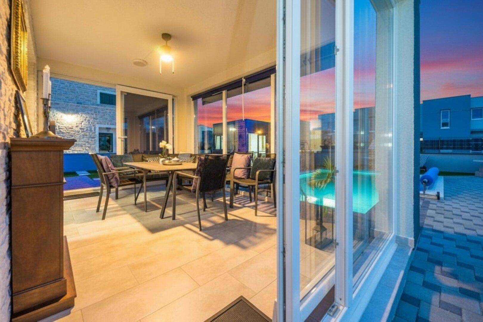 Heller Essbereich mit großen Glasfronten, die den Blick auf den Pool und den Sonnenuntergang freigeben.