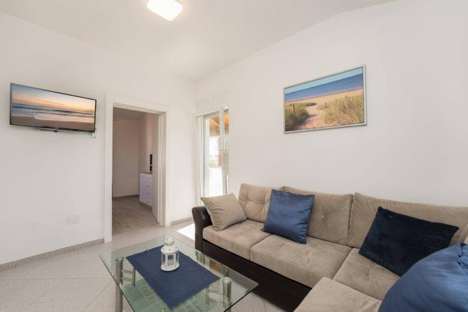 Gemütliches Wohnzimmer mit beigem Sofa, Couchtisch und Flachbildfernseher, hell und einladend.