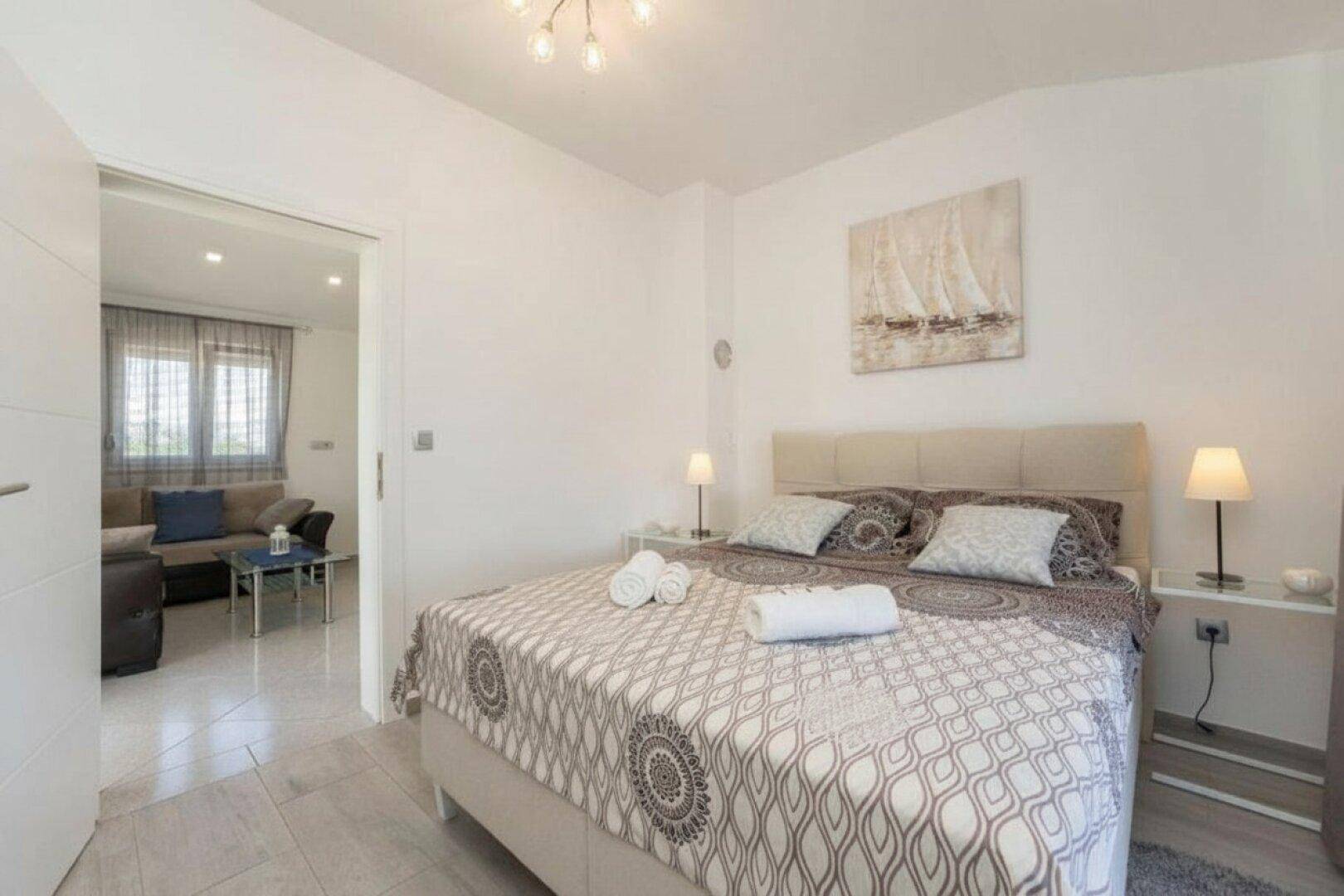 Helles Schlafzimmer mit Doppelbett, Nachttischen und Zugang zu einem weiteren Wohnbereich.