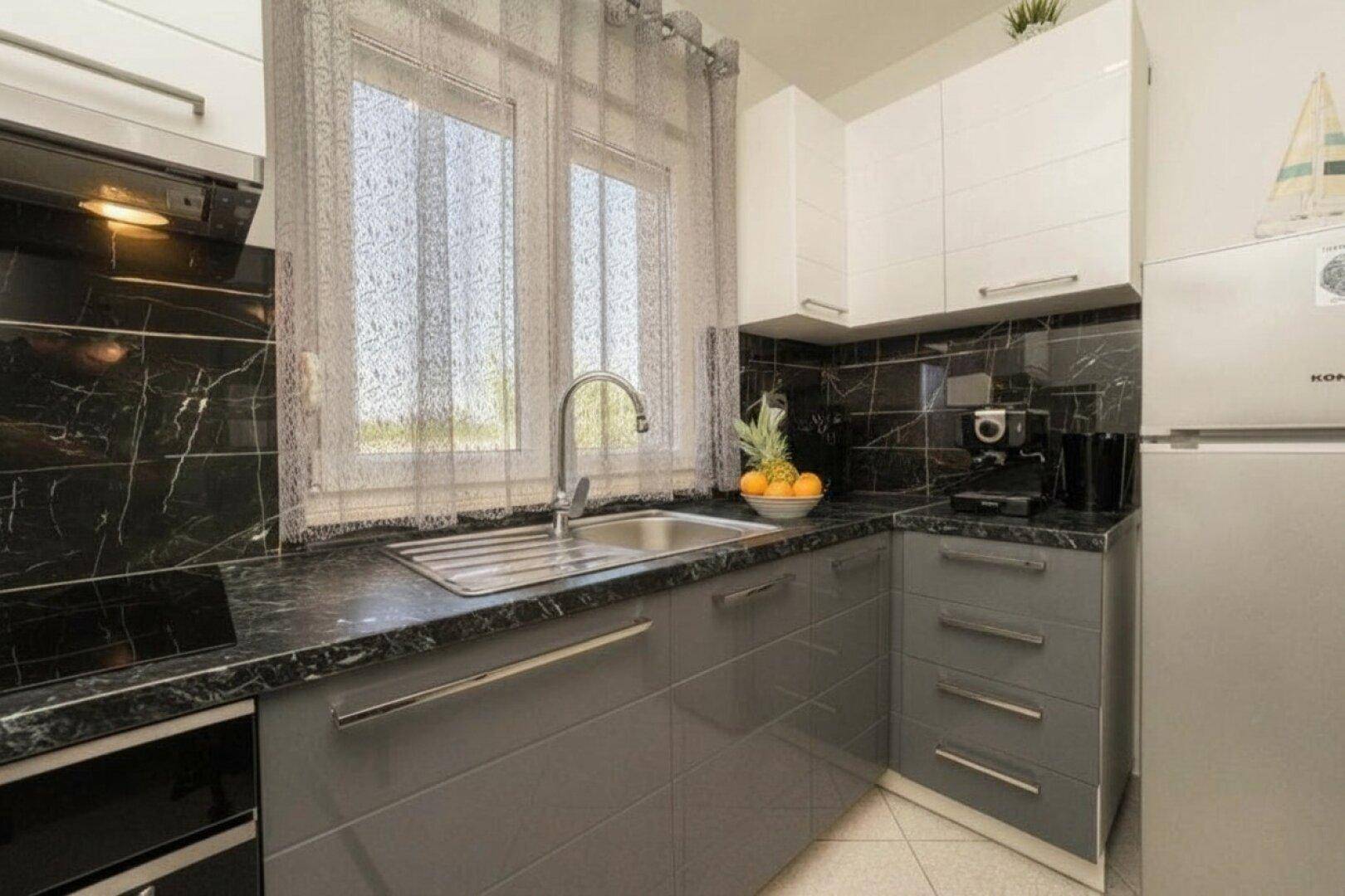 Moderne Küche mit grauen und weißen Hochglanzschränken, dunkler Arbeitsplatte und Fenster.