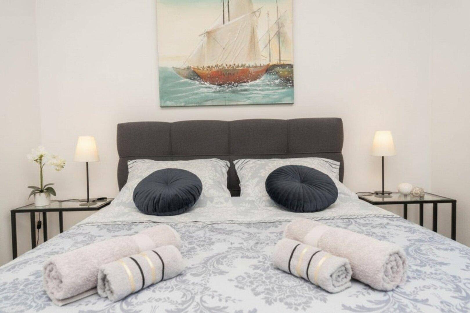 Komfortables Doppelbett mit dunklem Kopfteil und maritimer Kunst an der Wand.