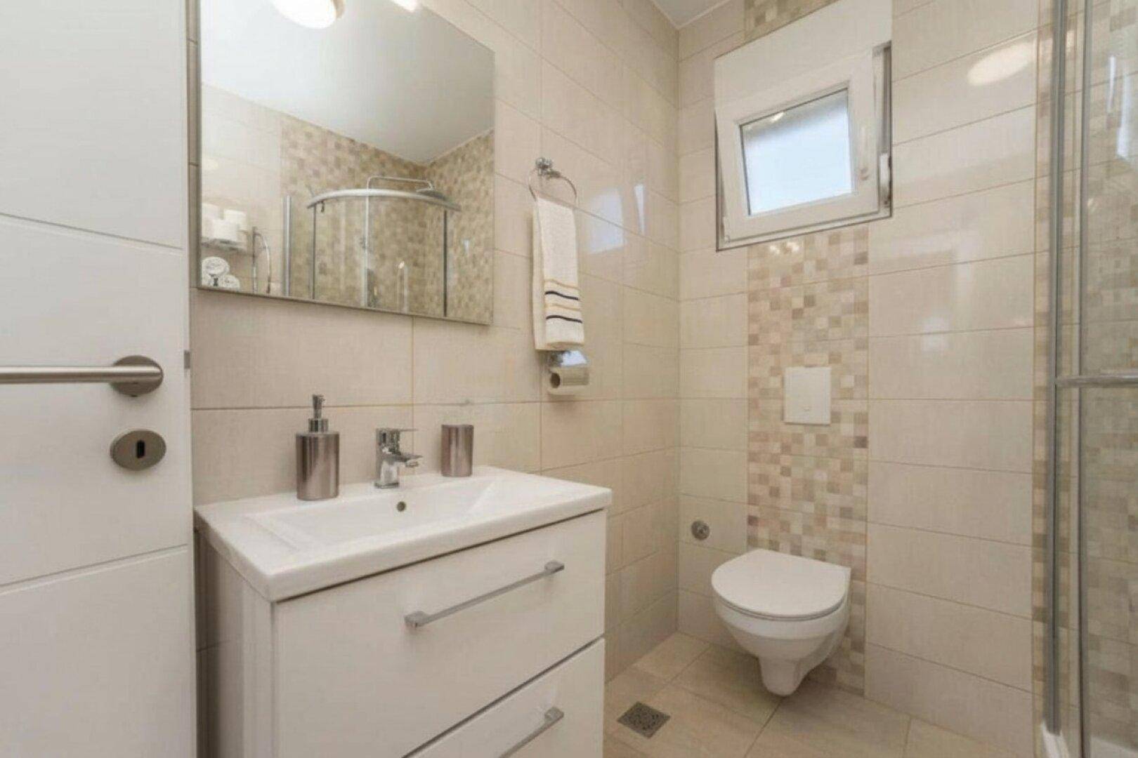 Modernes Badezimmer mit Waschtisch, wandhängendem WC, Duschkabine und Fenster.
