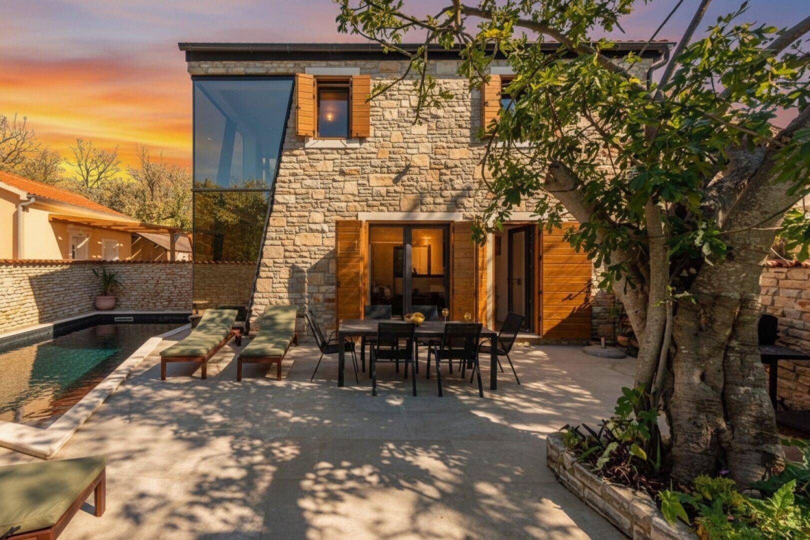 Geräumige Terrasse mit Esstisch und Stühlen, umgeben von Steinmauern und einem großen Baum.