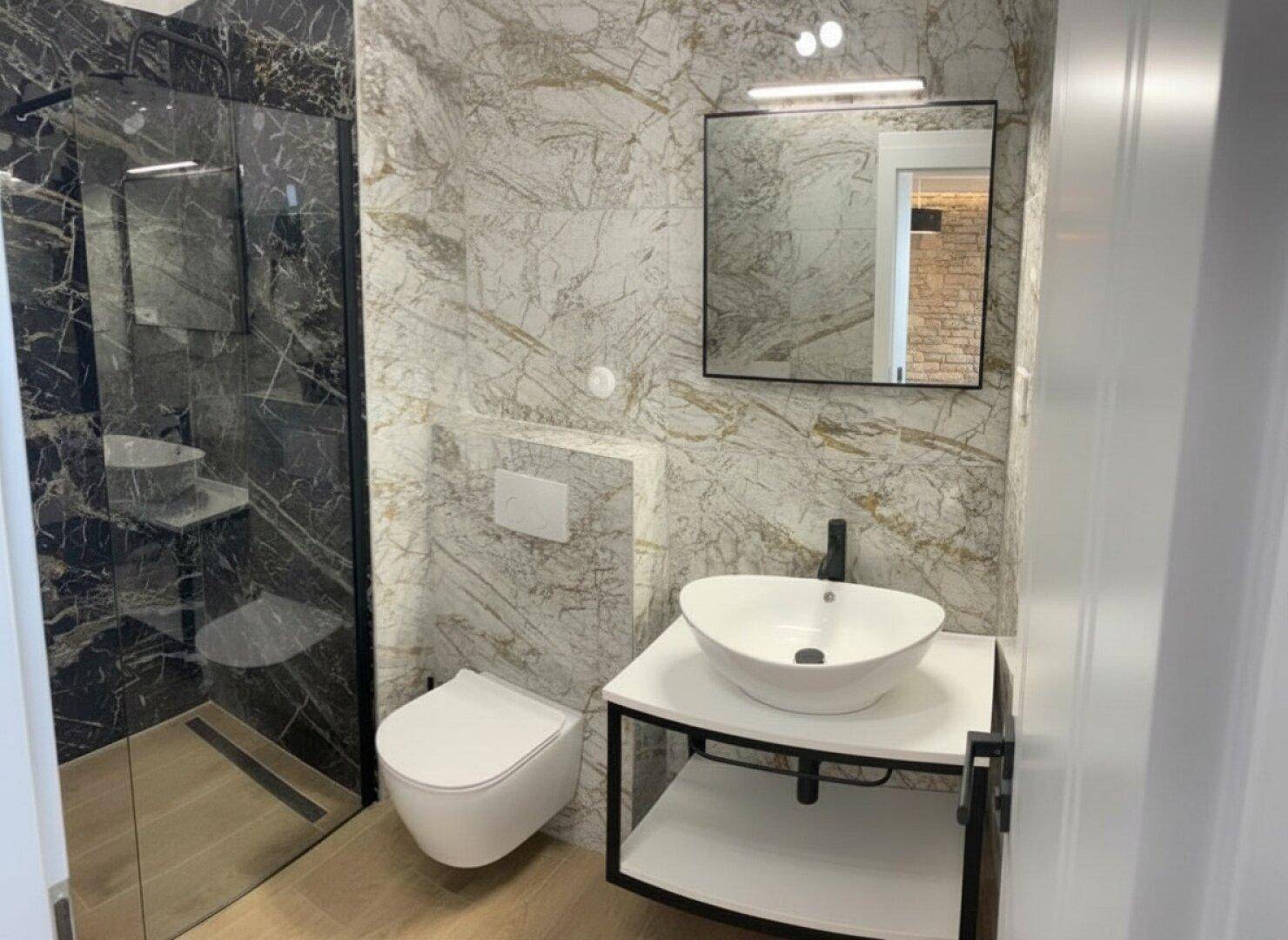 Modernes Badezimmer mit Marmorfliesen, begehbarer Dusche, wandhängendem WC und Aufsatzwaschbecken.