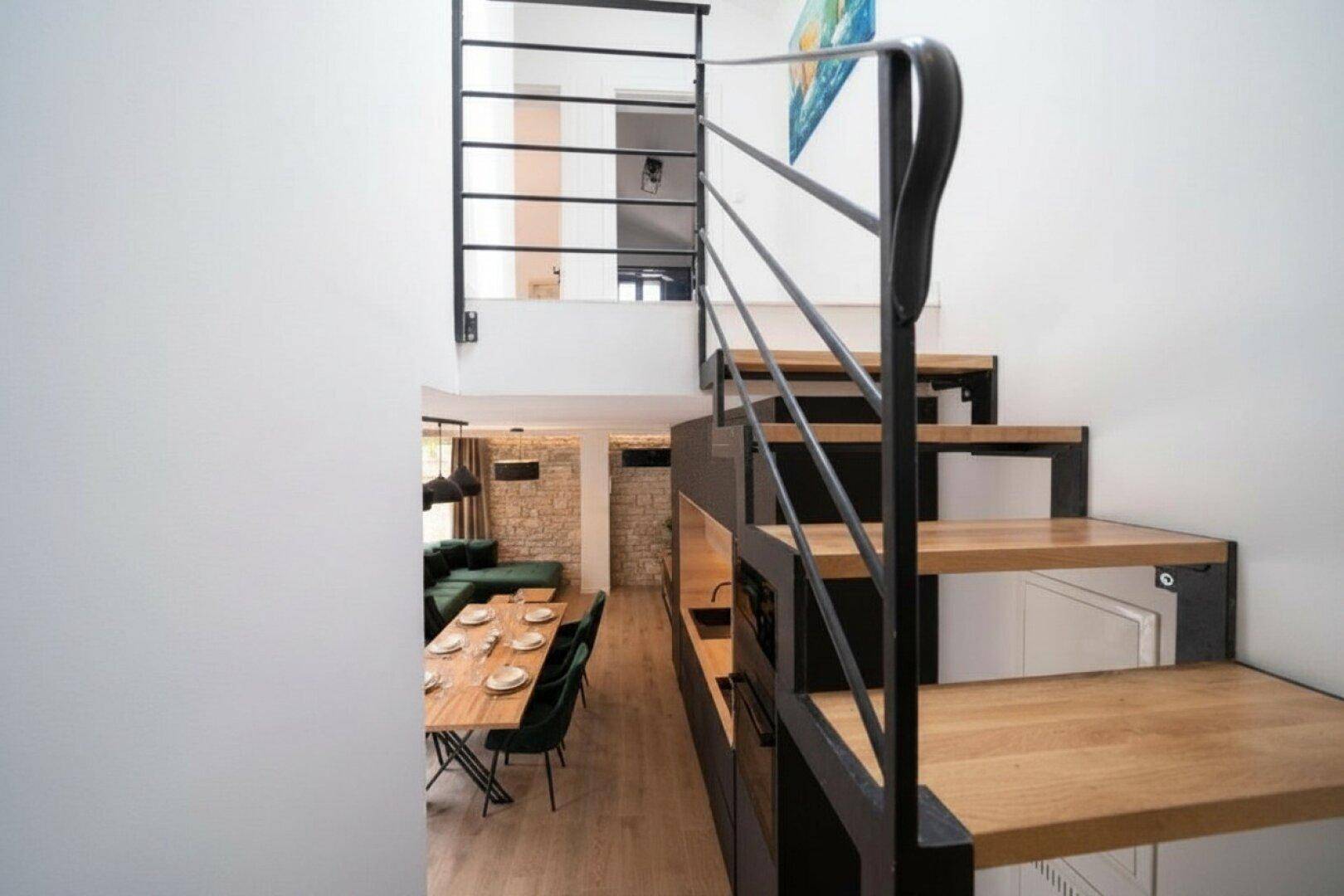 Moderne Treppe mit Holzstufen und Metallgeländer, die den Wohnbereich mit der oberen Etage verbindet.