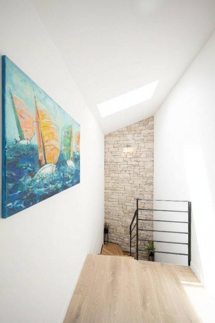 Treppenhaus mit Oberlicht, Steinwand und einem farbenfrohen Gemälde, das den Raum belebt.
