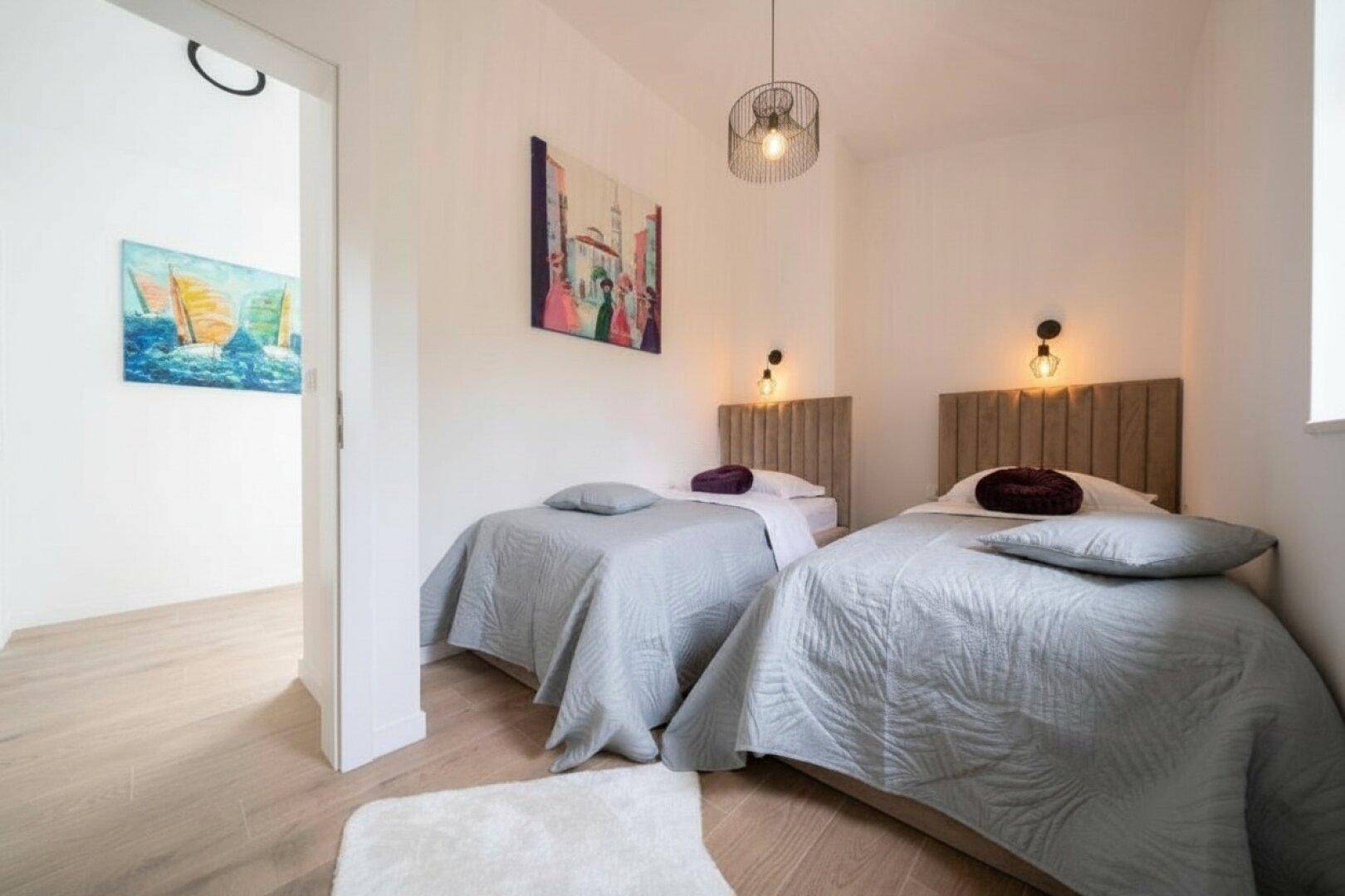 Helles Schlafzimmer mit zwei Einzelbetten, schlichter Einrichtung und einem Kunstwerk an der Wand.