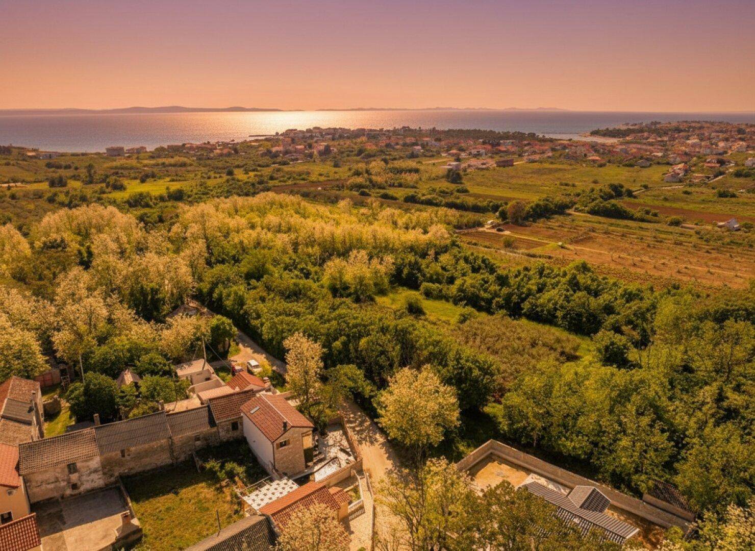 Luftaufnahme der Küstenlandschaft mit Häusern, grünen Feldern und dem Meer in der Ferne.