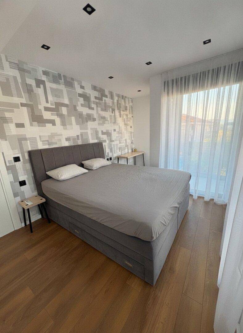 Helles Schlafzimmer mit großem Bett, Holzboden und dekorativer Wandgestaltung.