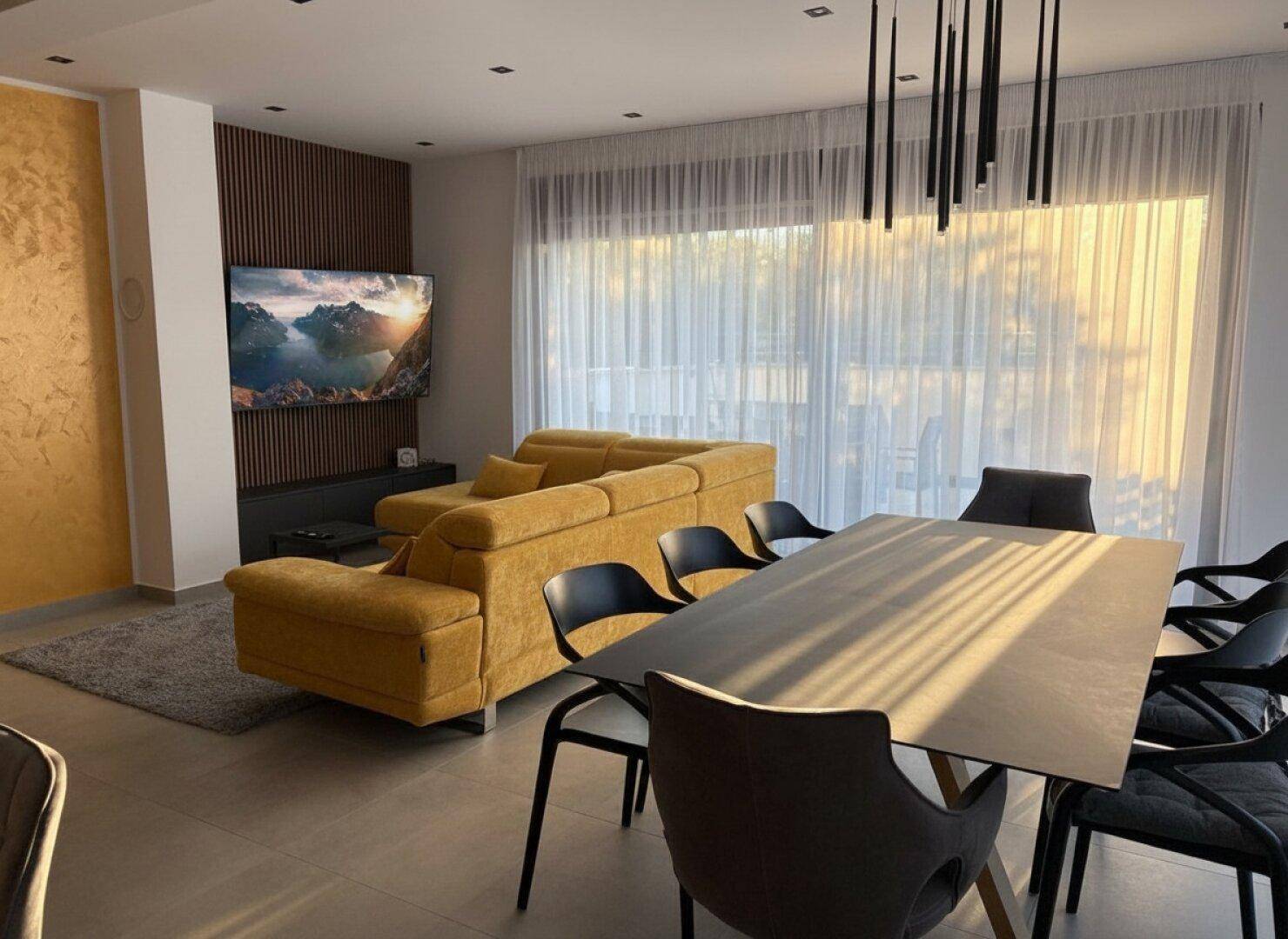 Heller Wohn- und Essbereich mit gelbem Ecksofa, modernem Esstisch und großen Fenstern.