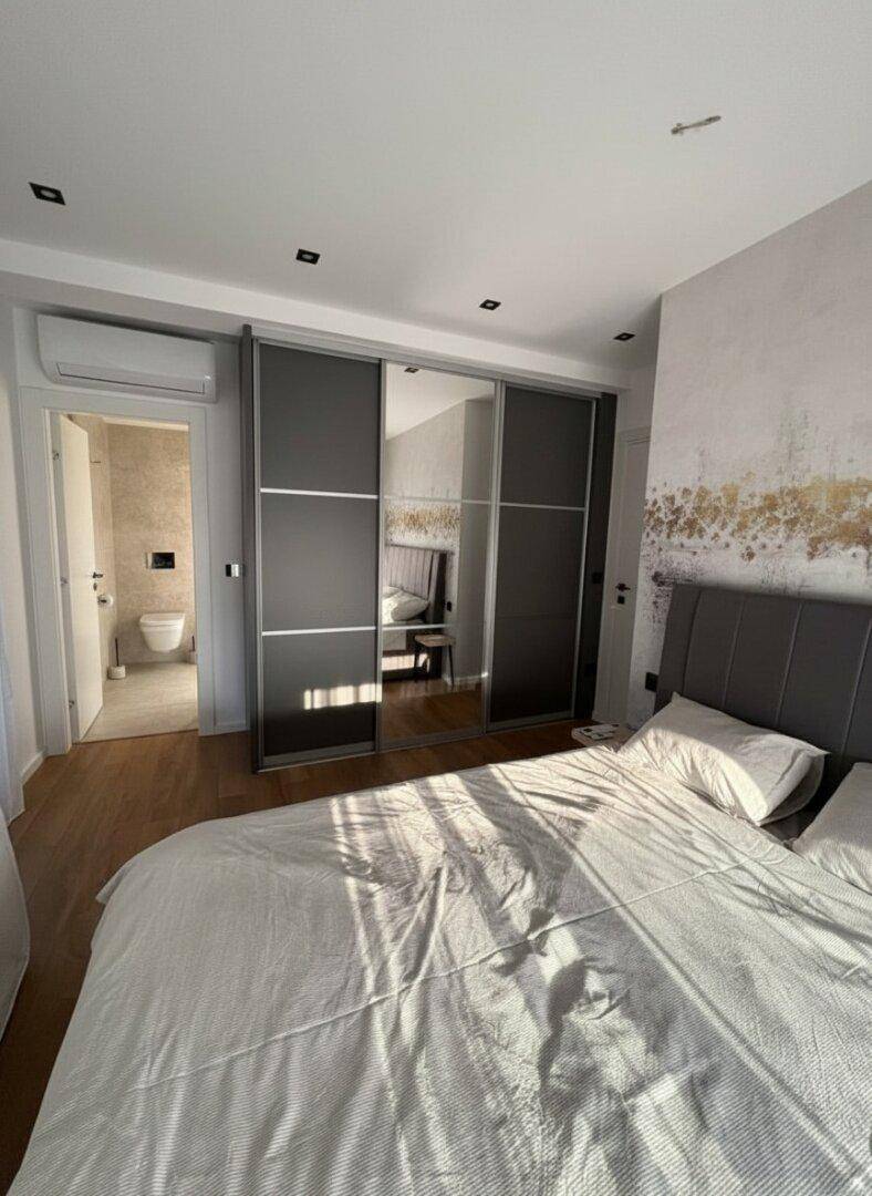 Schlafzimmer mit großem Bett, Spiegelschränken und Zugang zu einem modernen Badezimmer.