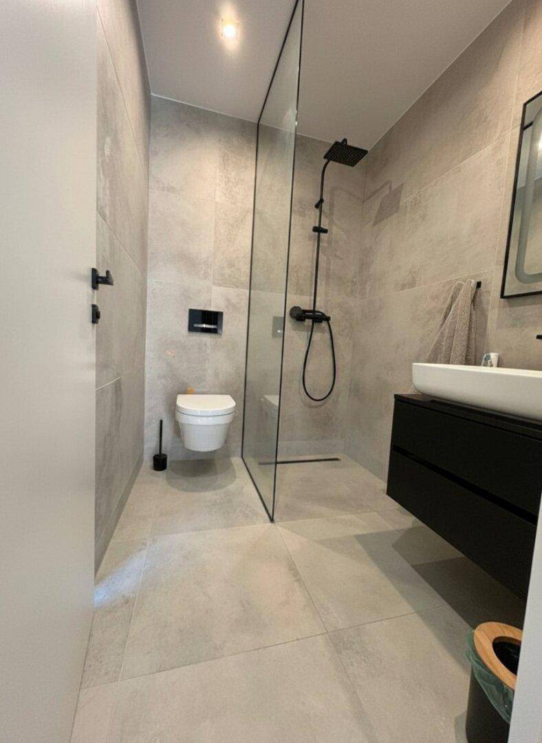 Modernes Badezimmer mit begehbarer Dusche, Wand-WC und eleganten grauen Fliesen.