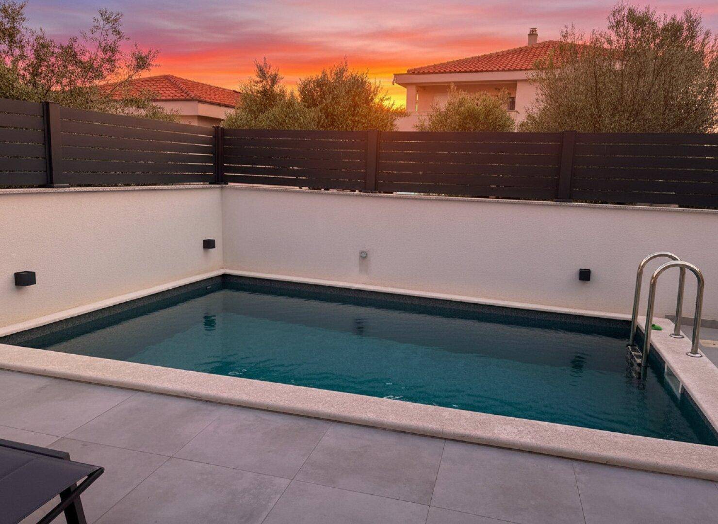 Privater Swimmingpool im Außenbereich mit gefliestem Rand und Sonnenuntergangshimmel.