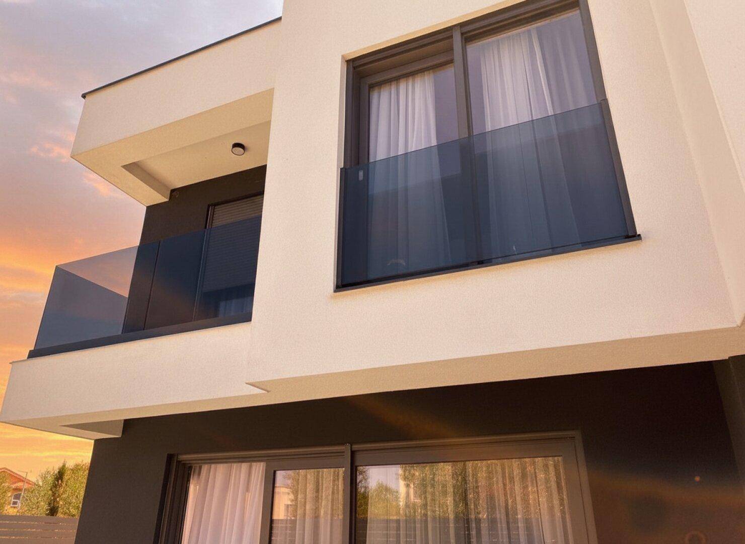Moderner Balkon mit Glasgeländer an der Fassade des Gebäudes bei Sonnenuntergang.