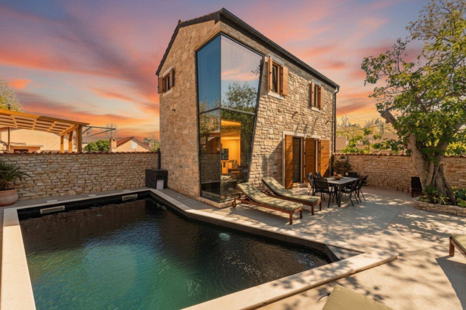 Charmantes Steinhaus mit modernem Glasanbau, privatem Pool und möblierter Terrasse unter einem farbenfrohen Sonnenuntergang.