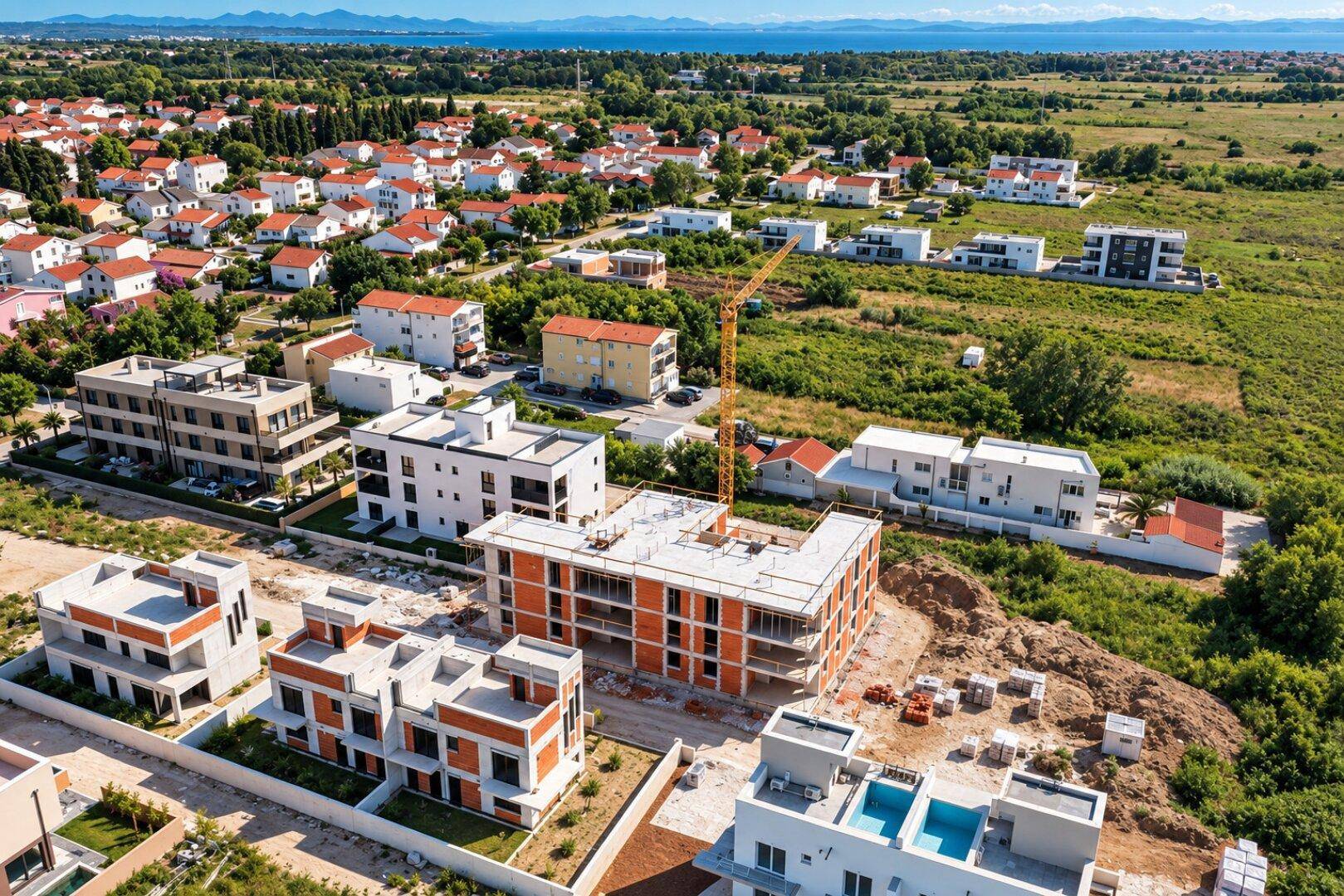 Luftaufnahme einer Wohnsiedlung im Bau mit Blick auf das Meer und umliegende Häuser.