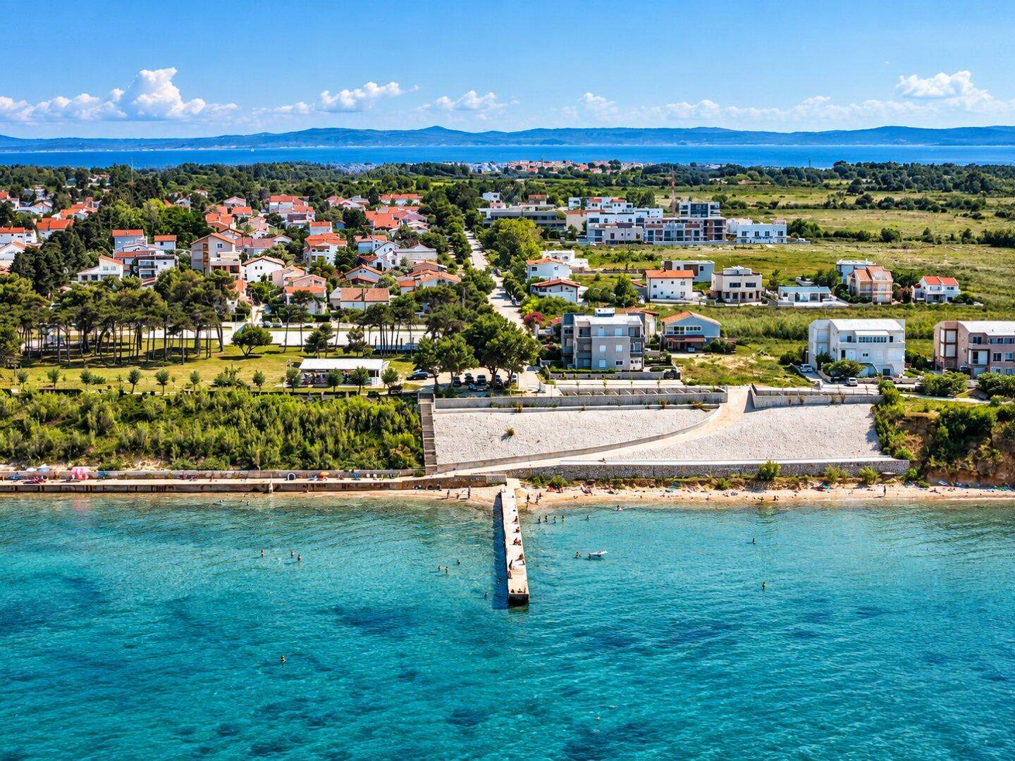 Atemberaubende Luftaufnahme einer Küstenlandschaft mit türkisblauem Wasser, Strand und Wohngebiet.