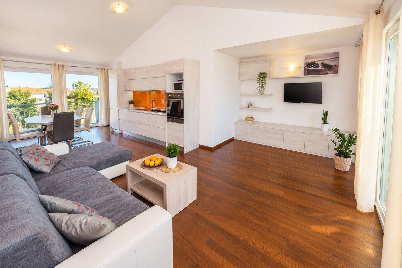 Heller Wohnbereich mit offener Küche, Holzboden und Zugang zu einem Balkon mit Aussicht.