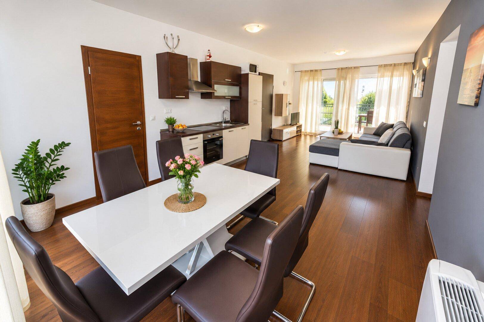 Offener Wohn- und Essbereich mit kleiner Küche, Holzboden und Zugang zum Balkon.