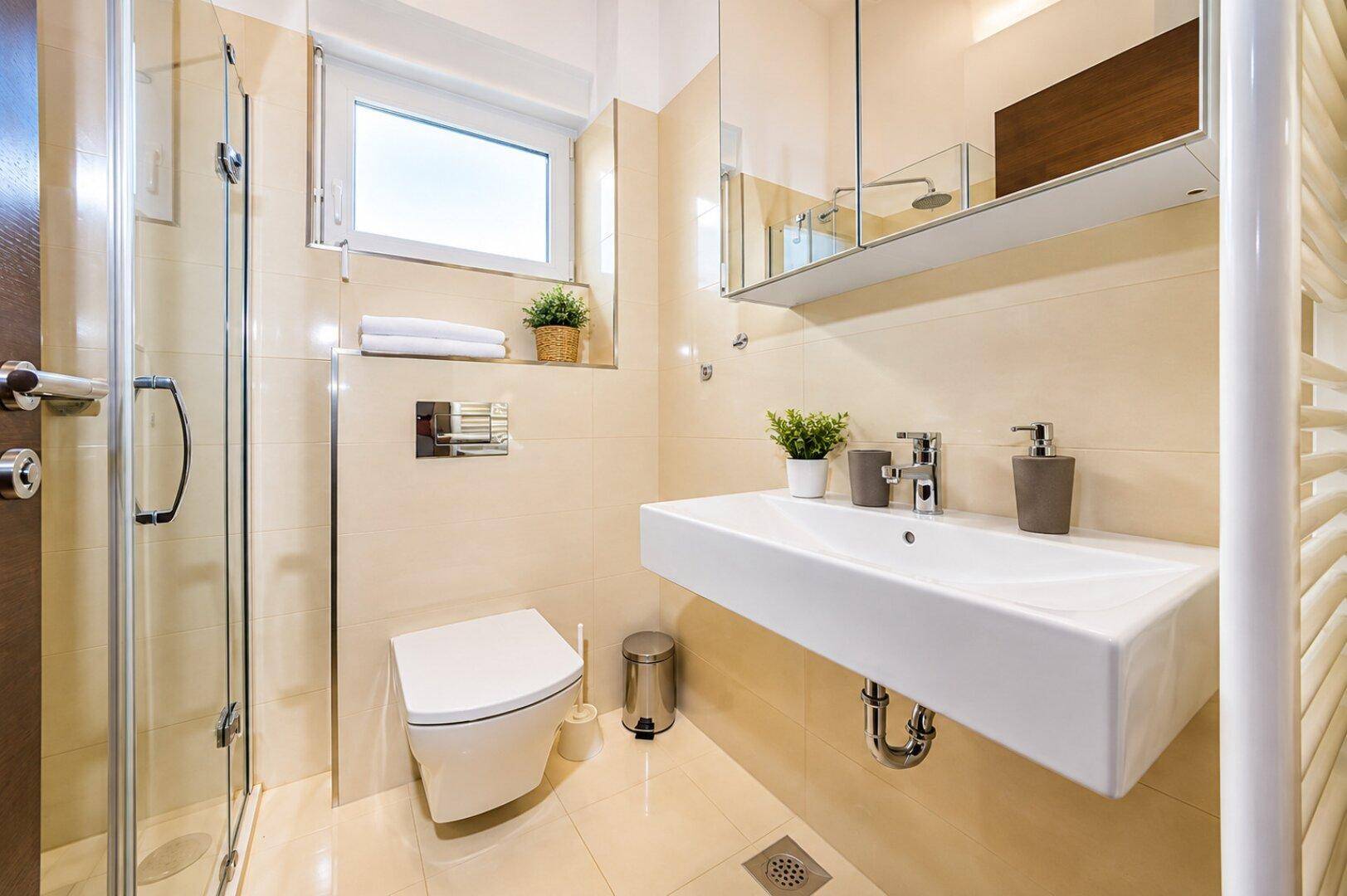 Modernes Badezimmer mit beigefarbenen Fliesen, schwebendem Waschbecken und Duschkabine.