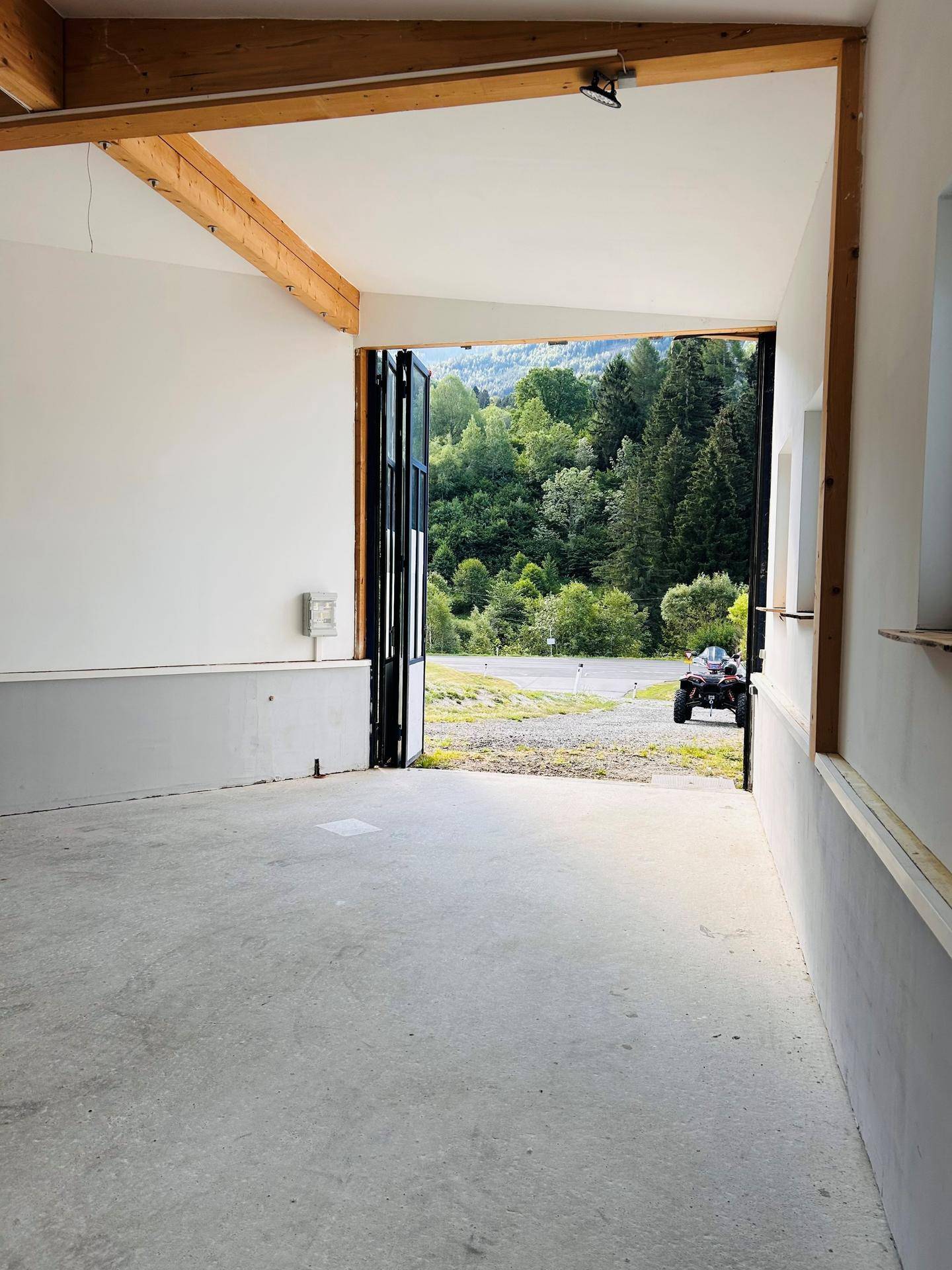 Heller Innenraum mit Blick durch die offene Tür auf eine grüne Berglandschaft und einen Feldweg.