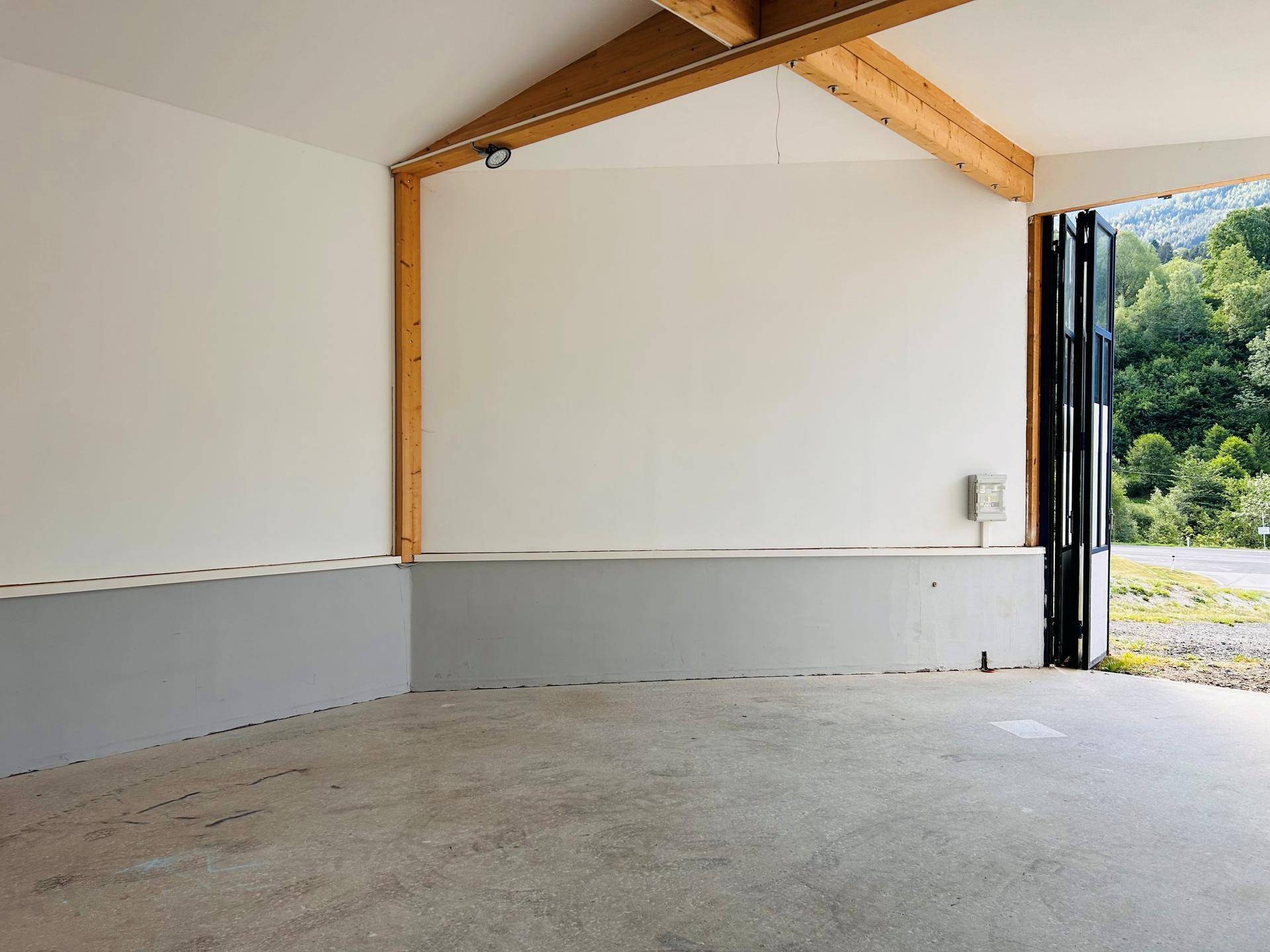 Geräumiger Innenraum mit hohen Decken, Holzbalken und einem Betonboden, der zur Landschaft hin offen ist.