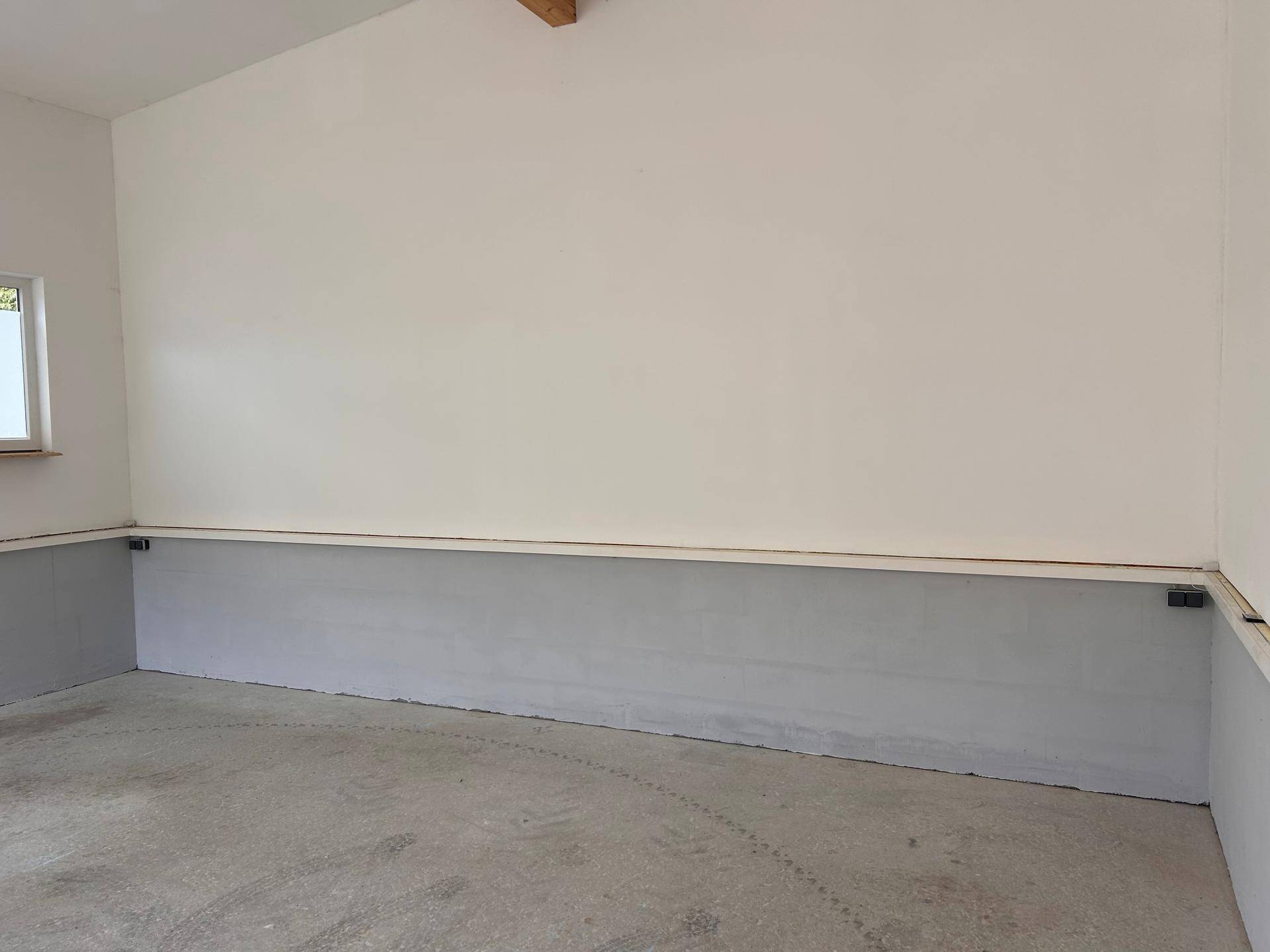 Heller Innenraum mit weißen Wänden, einem grauen Sockel und einem robusten Betonboden, ideal für Lagerung.