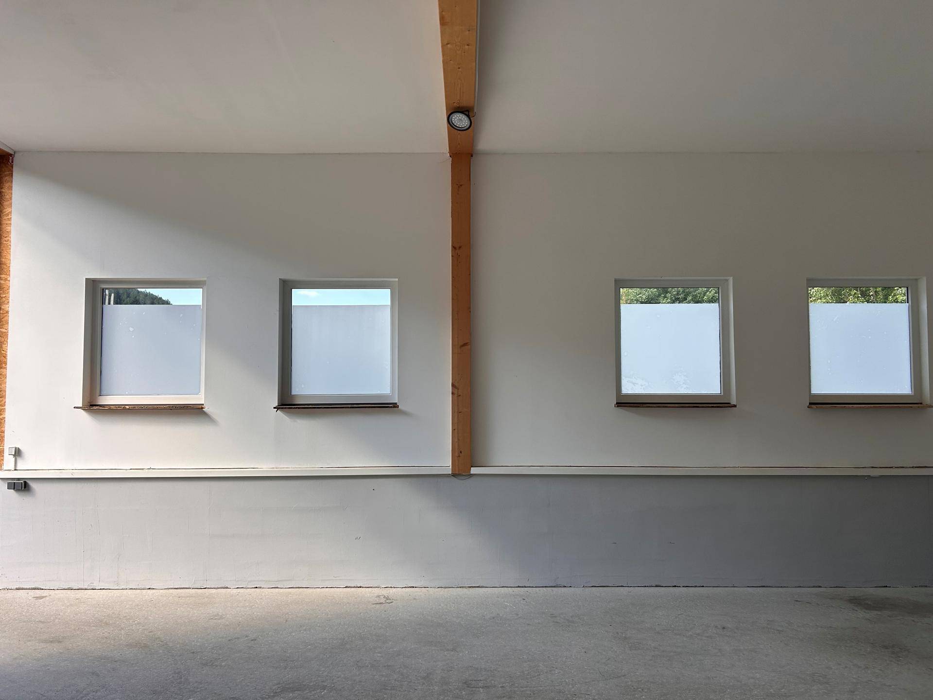 Innenansicht eines Raumes mit mehreren Fenstern, die natürliches Licht hereinlassen, und einem glatten Betonboden.