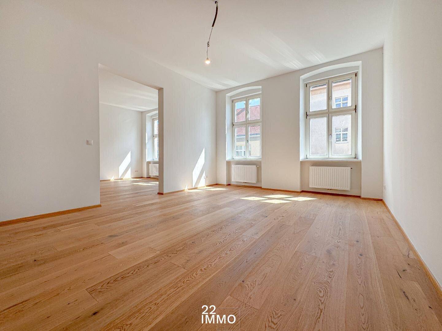 Geräumiger, heller Wohnbereich mit Holzboden und hohen Fenstern, ideal für offene Gestaltung.