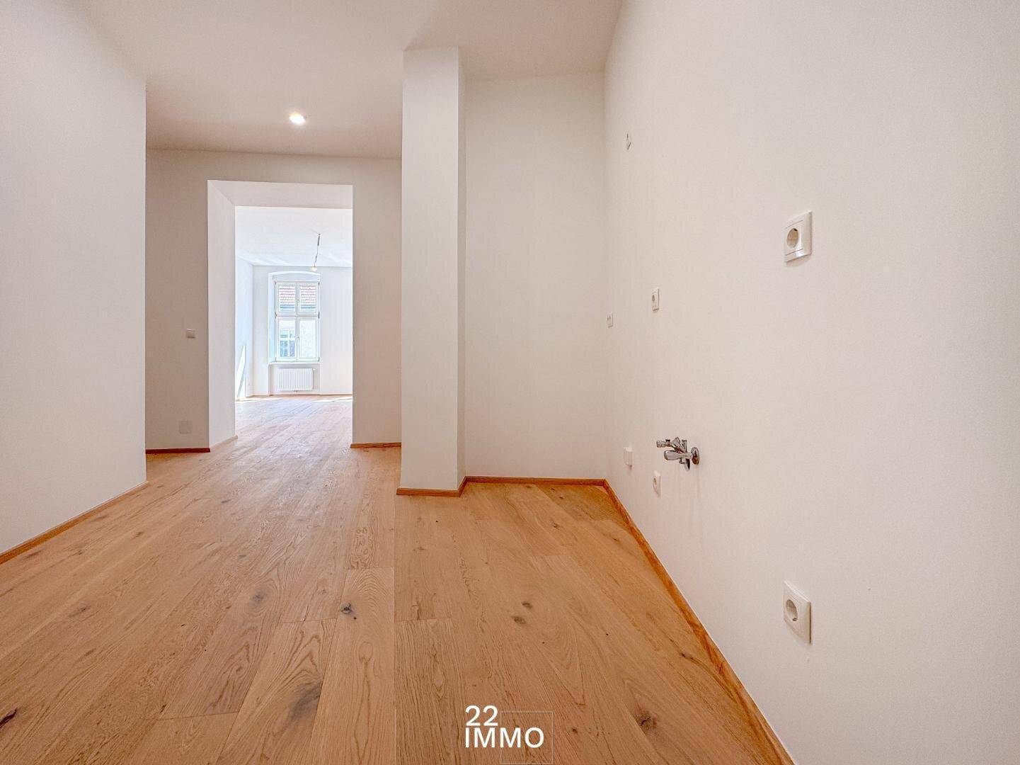 Leerer Küchenbereich mit Anschlüssen und Holzboden, bereit für den Einbau einer Küche.