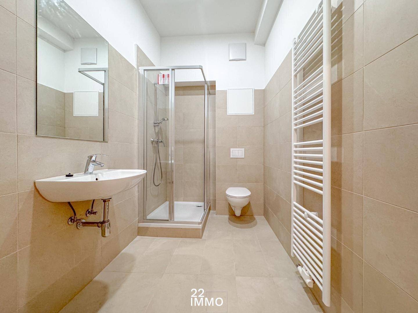 Modernes Badezimmer mit beigefarbenen Fliesen, Dusche und beheiztem Handtuchhalter.