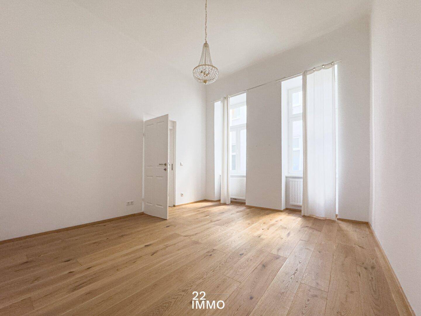 Heller Raum mit Parkettboden, hohen Decken und einem Kronleuchter, ideal als Schlafzimmer oder Arbeitszimmer.