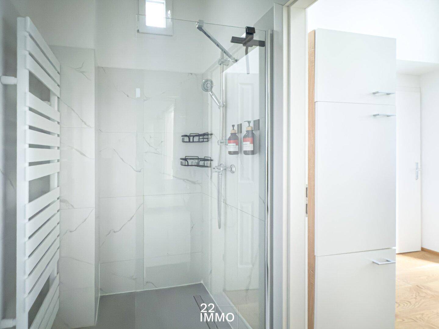 Modernes Badezimmer mit begehbarer Dusche, eleganten Marmorfliesen und beheiztem Handtuchhalter.