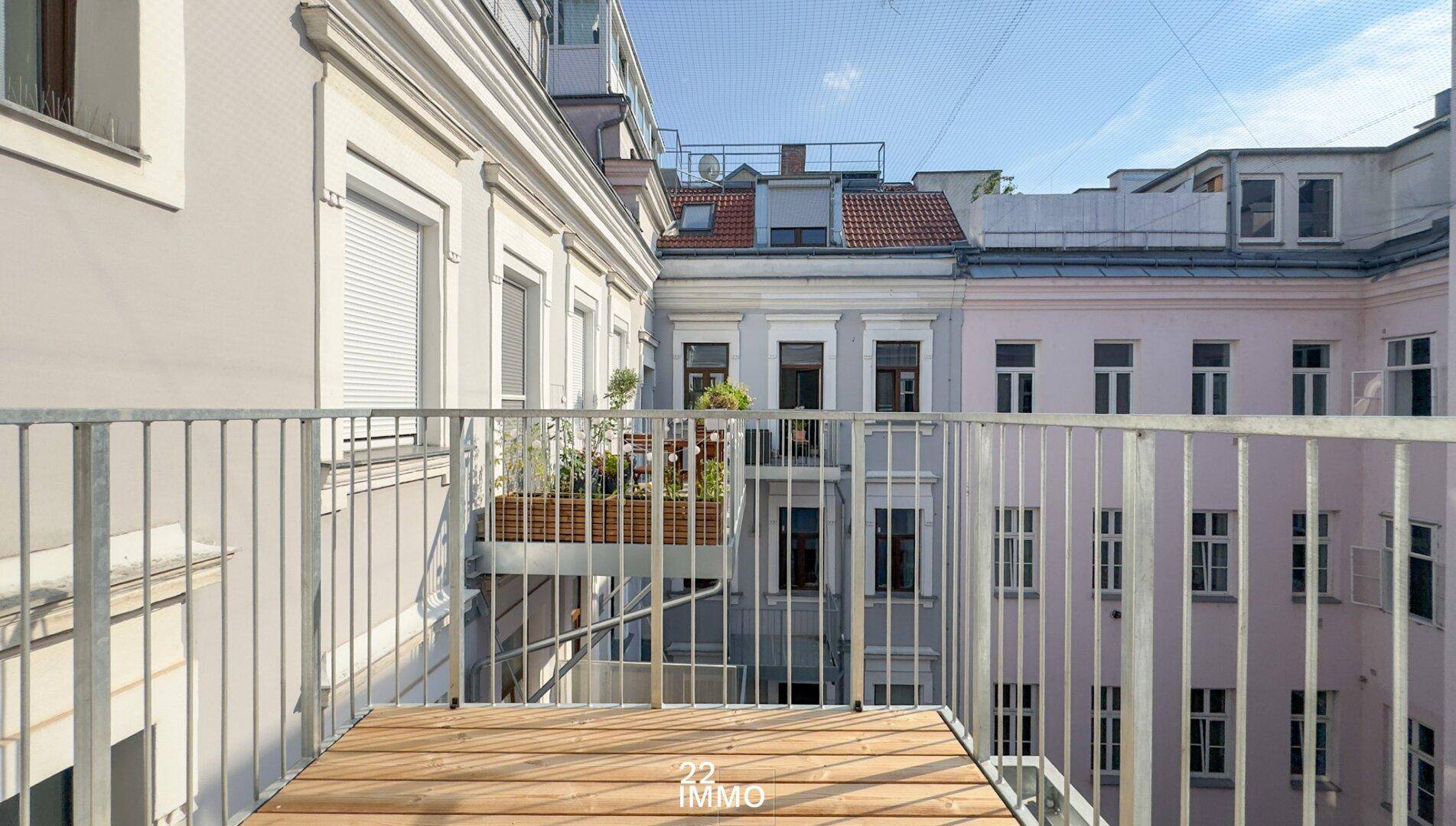 Leerer Balkon mit Holzboden und Metallgeländer, bietet Blick auf die umliegenden Gebäude.