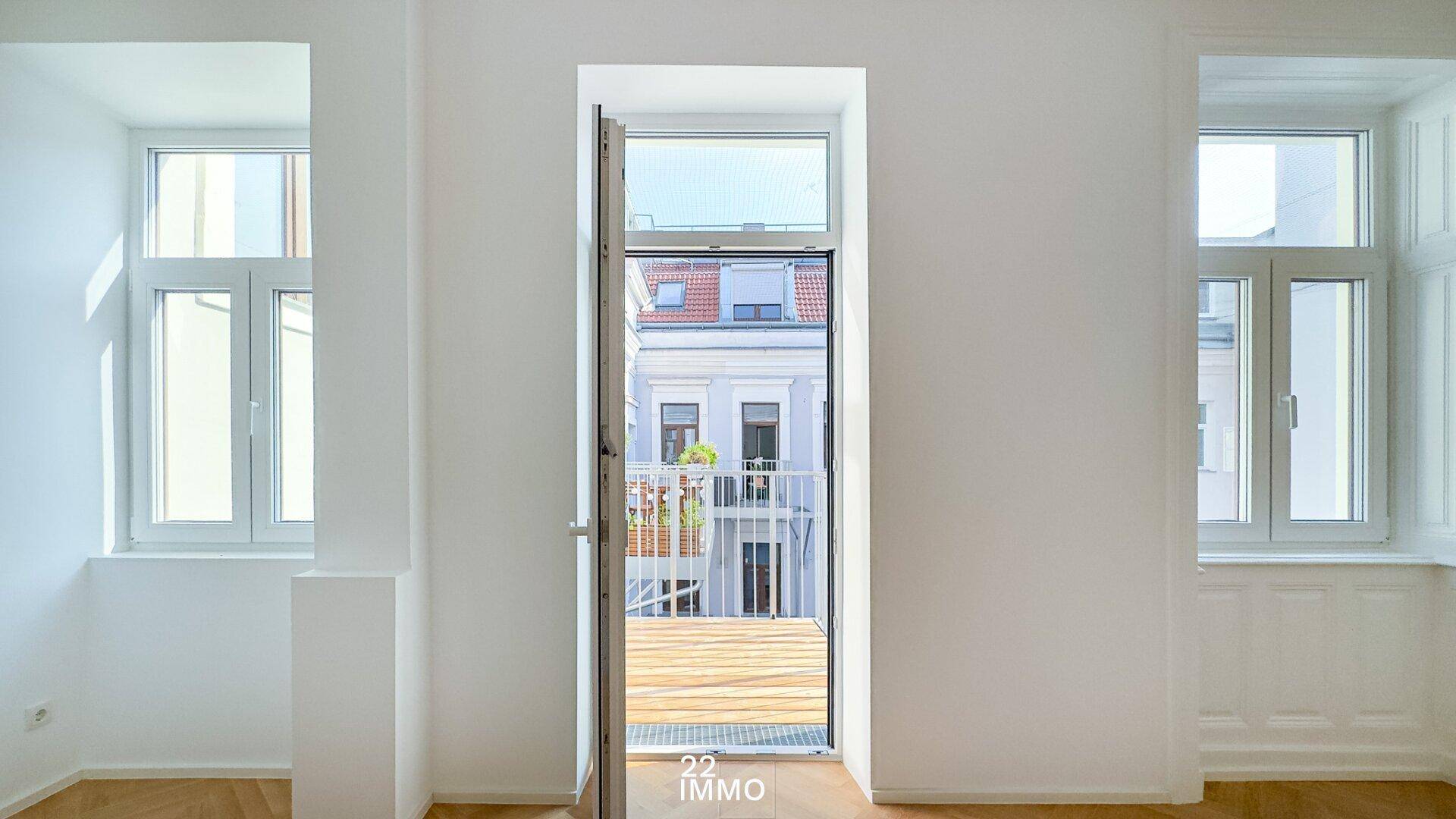 Heller Innenraum mit Zugang zu einem Balkon und Blick auf die Stadt.