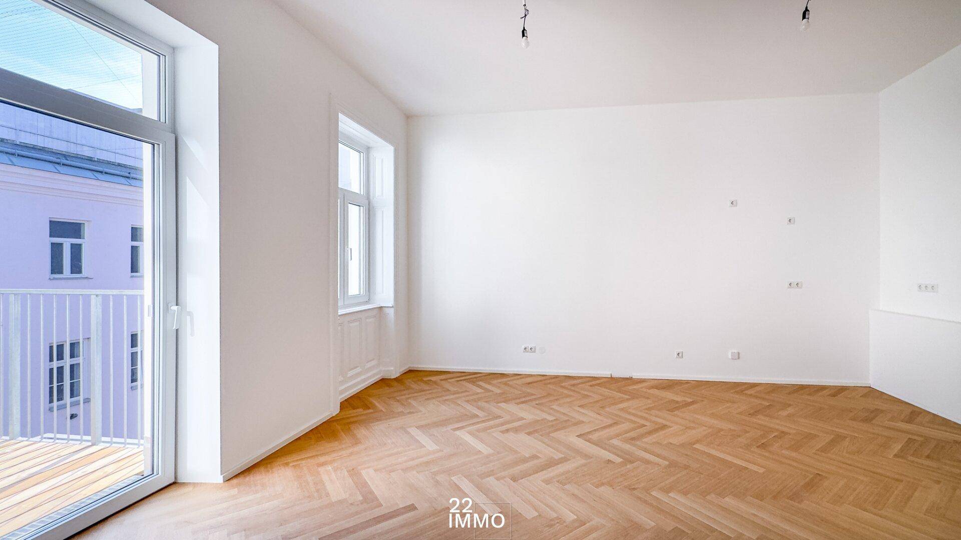 Leerer Raum mit Fischgrätparkett und großem Fenster mit Balkonzugang.