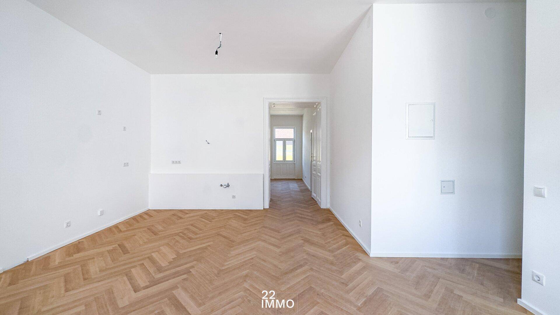 Geräumiger, leerer Raum mit Fischgrätparkett und Durchgang zu einem weiteren Zimmer.