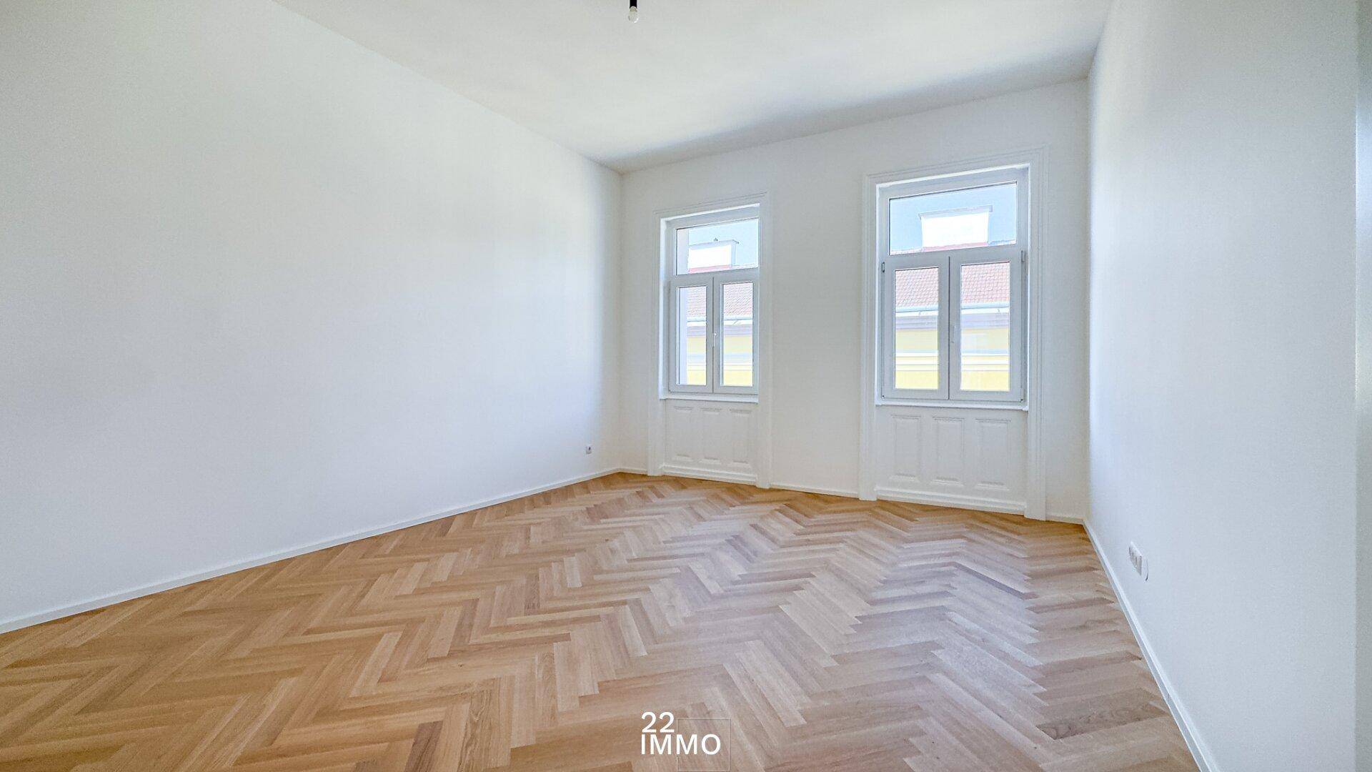 Heller, leerer Raum mit Fischgrätparkett und zwei Fenstern, ideal als Schlafzimmer.