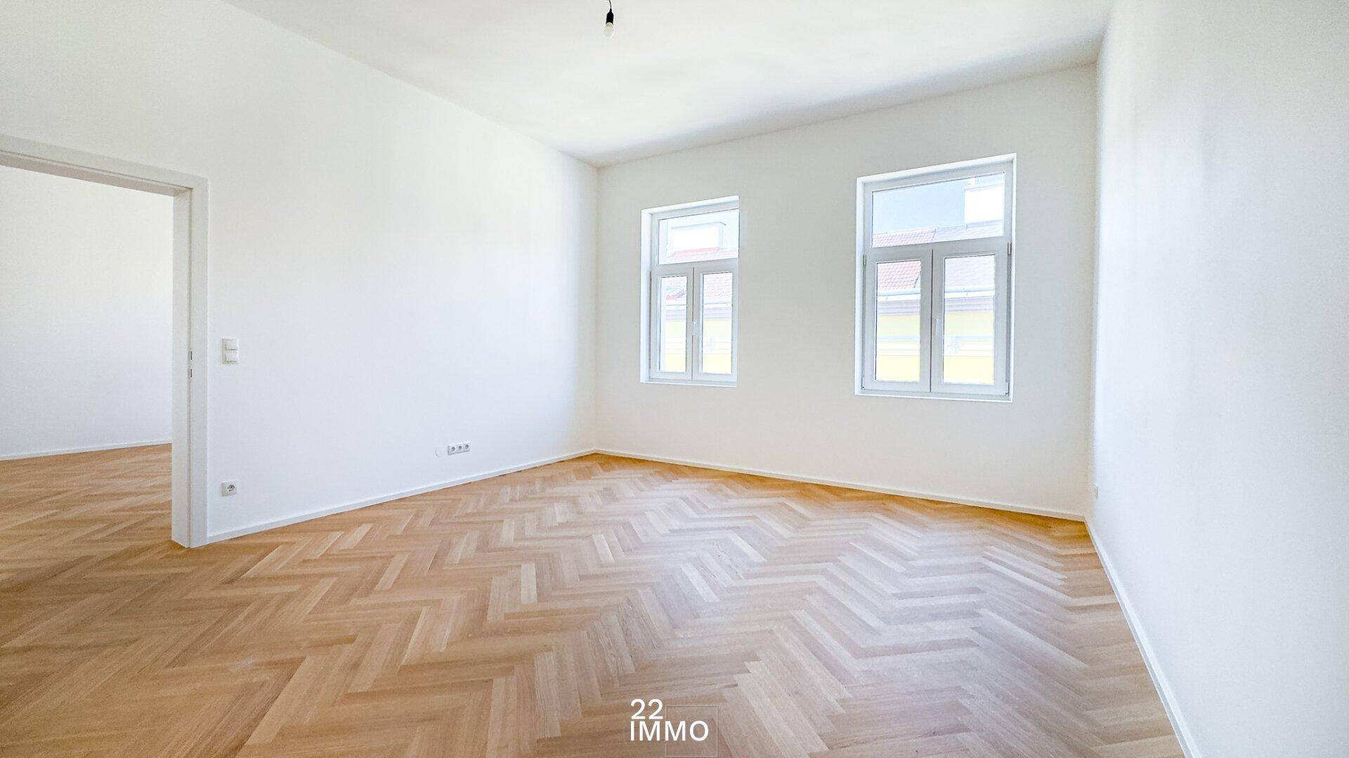 Geräumiger, leerer Raum mit Fischgrätparkett und Zugang zu einem weiteren Zimmer.