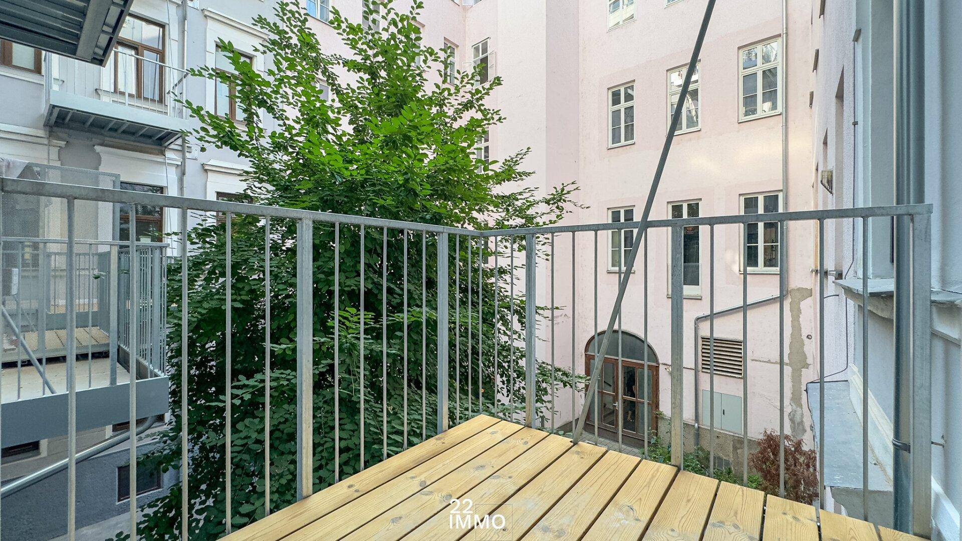 Kleiner Balkon mit Holzboden und Metallgeländer, bietet einen Blick auf den Innenhof.