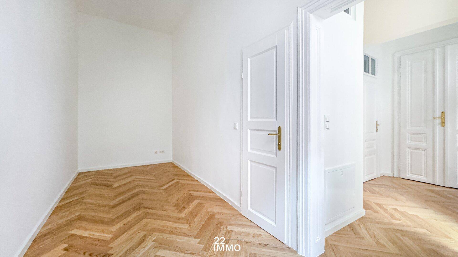 Helles, leeres Zimmer mit Fischgrätparkett und einer klassischen weißen Tür, bereit zur Einrichtung.