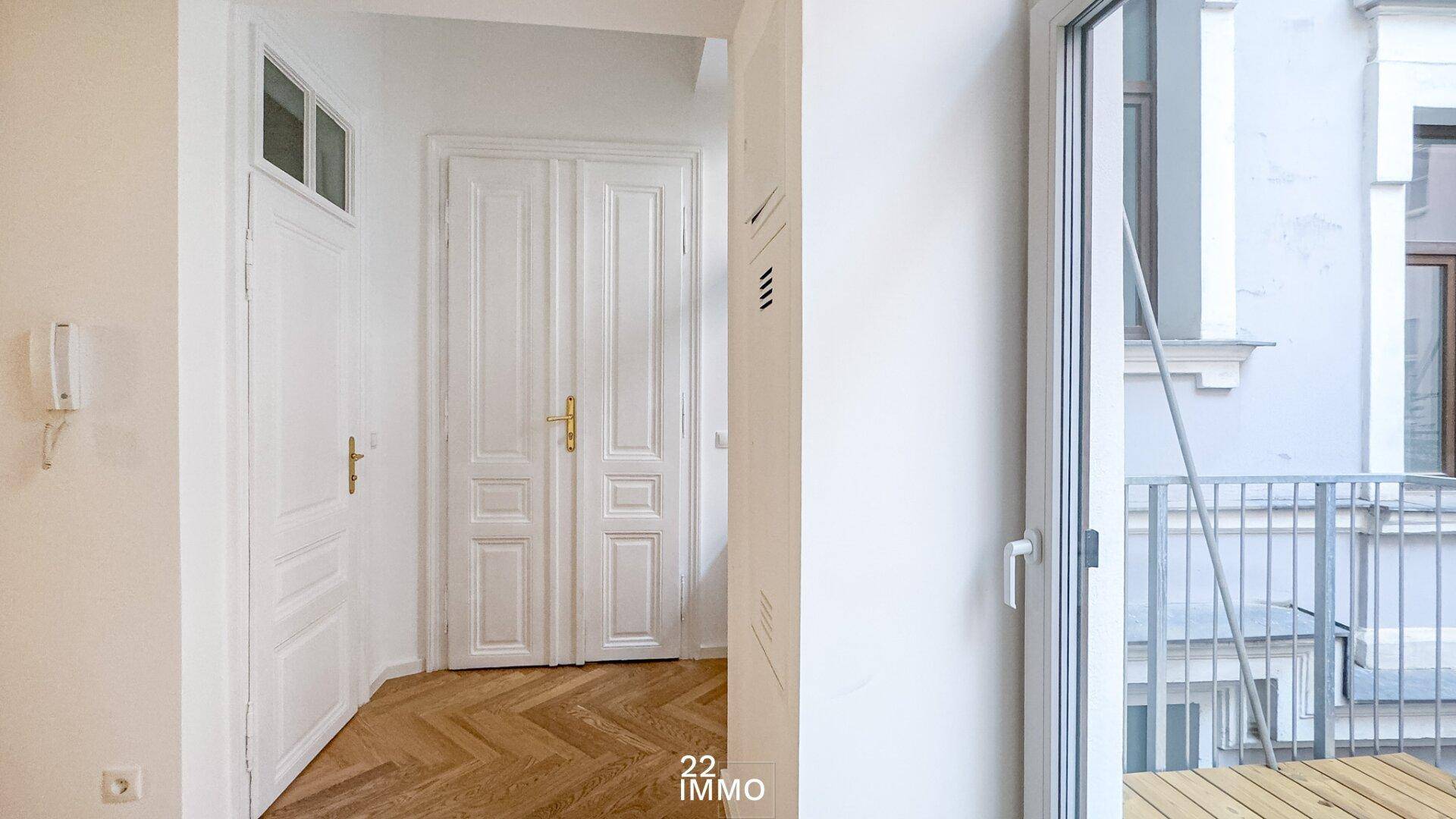 Heller Flur mit Fischgrätparkett und klassischen weißen Doppeltüren, mit Zugang zu einem Balkon.
