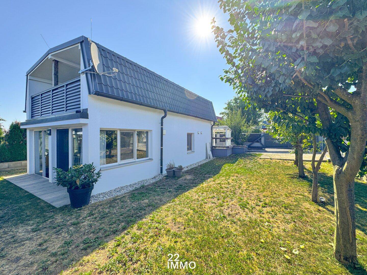 Seitenansicht des Hauses mit weißer Fassade, dunklem Dach und einem gepflegten Garten mit Bäumen.