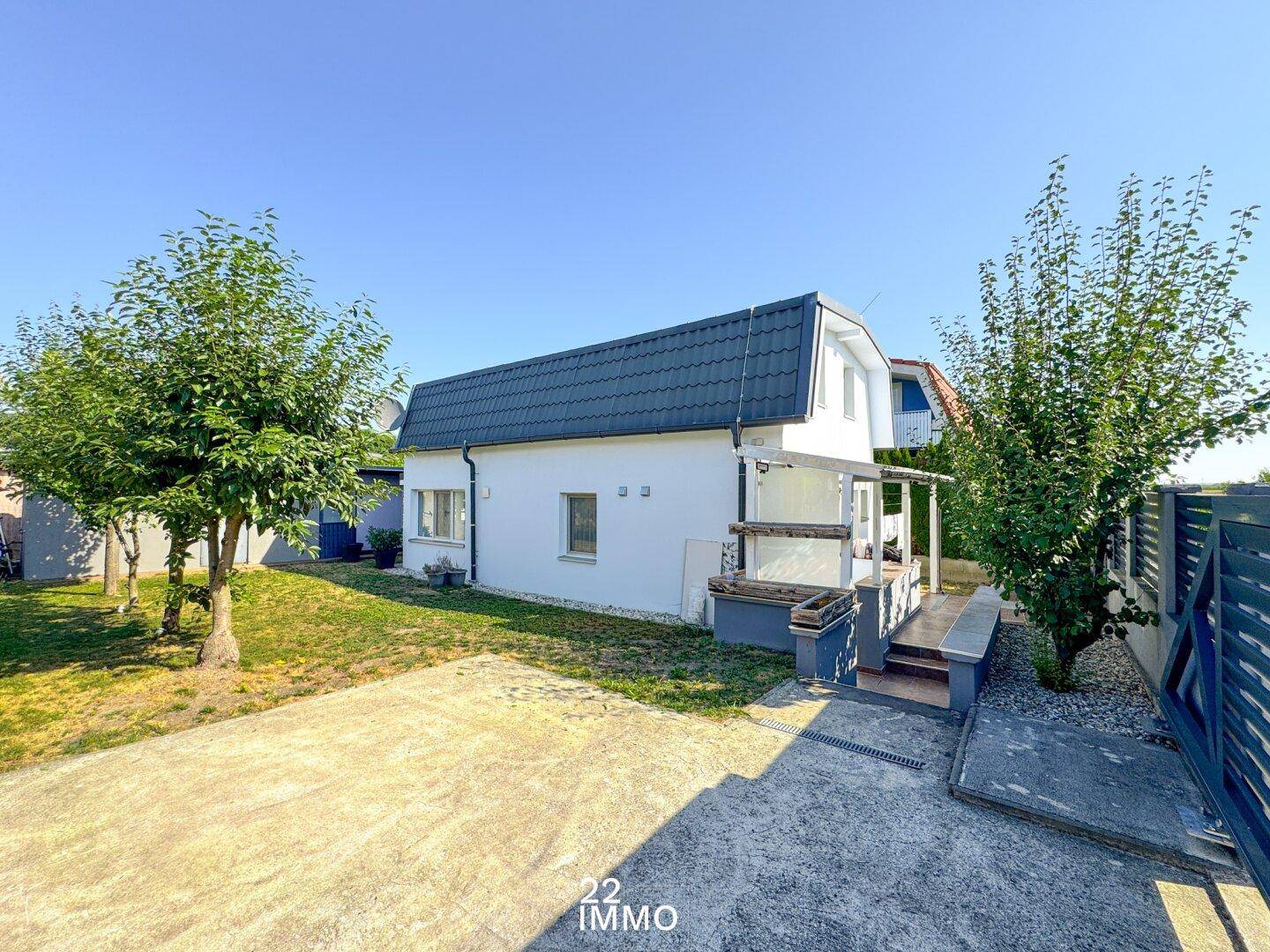 Vorderansicht des Hauses mit Zufahrt und einem kleinen Vorgarten unter strahlend blauem Himmel.