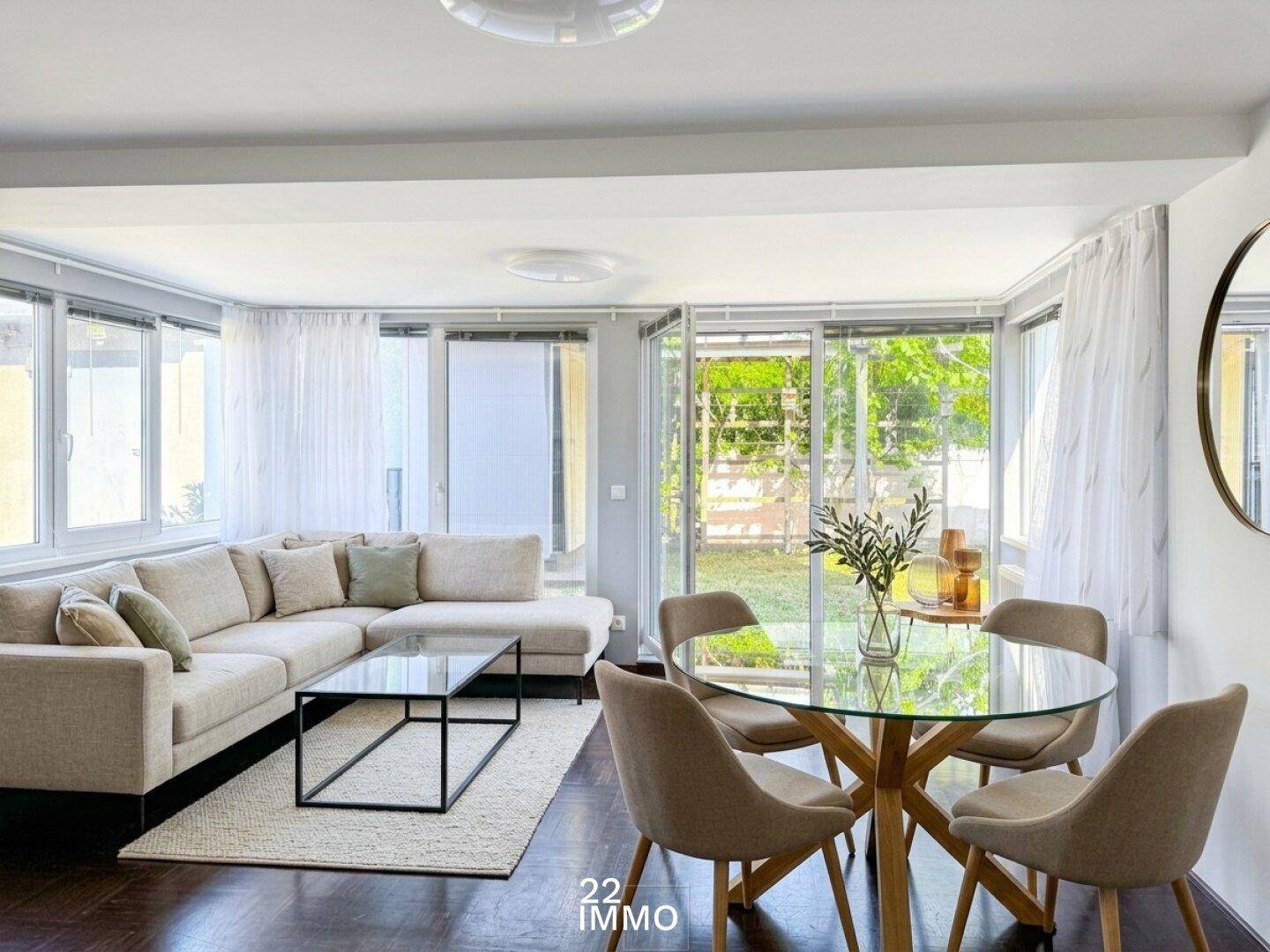 Gemütlicher Wohn- und Essbereich mit großzügigen Fenstern, hellem Sofa und modernem Esstisch.
