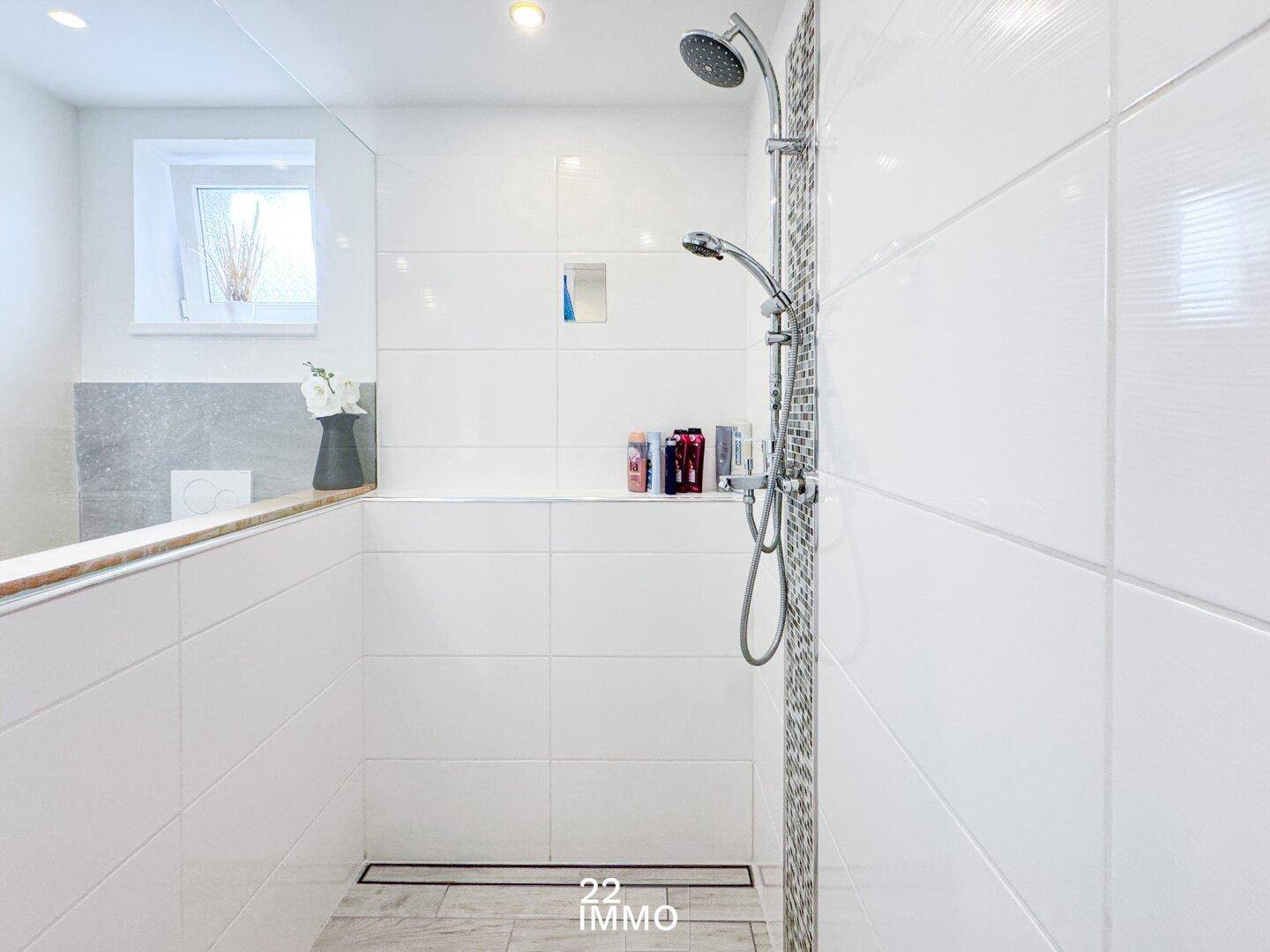 Helles Badezimmer mit moderner begehbarer Dusche, weißen Fliesen und Fenster für Tageslicht.