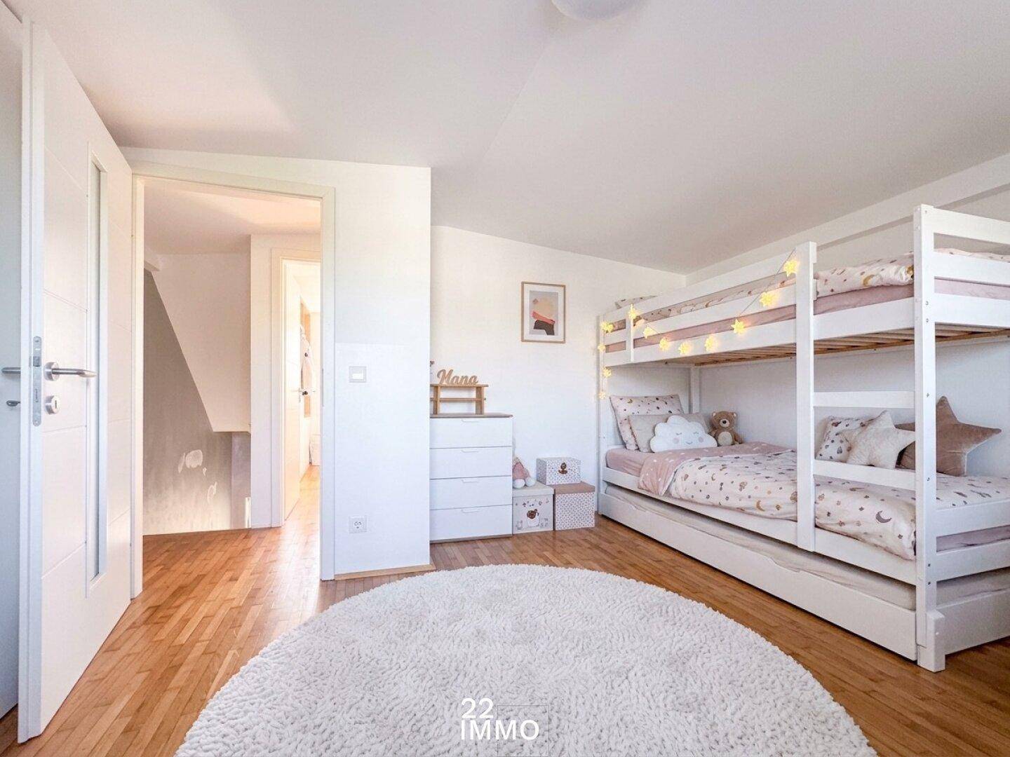 Kinderzimmer mit Etagenbett, hellem Holzboden und einem weichen Teppich, freundlich eingerichtet.